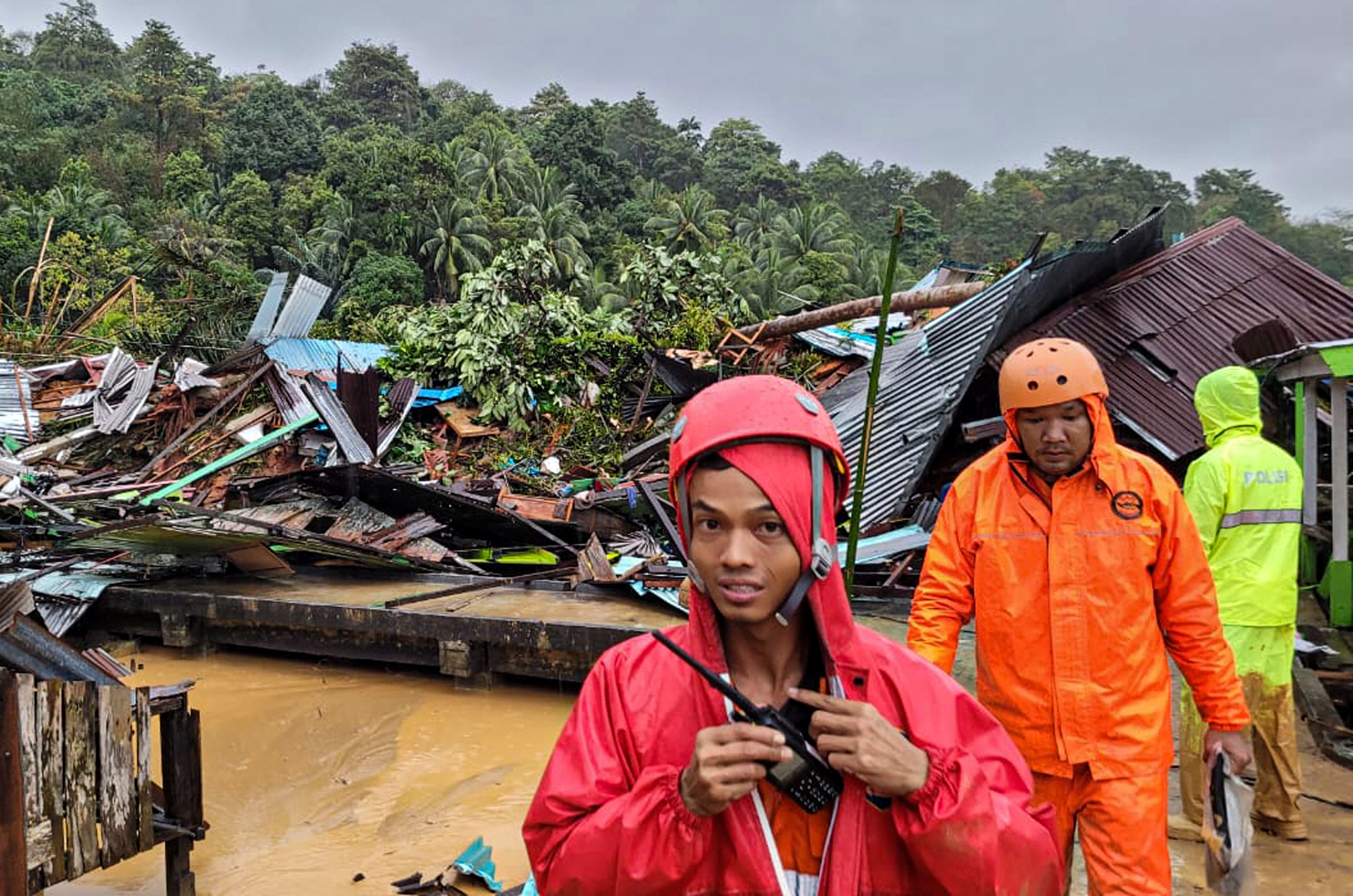 Indonesian rescue members stand near damaged houses affected by a landslide in Natuna