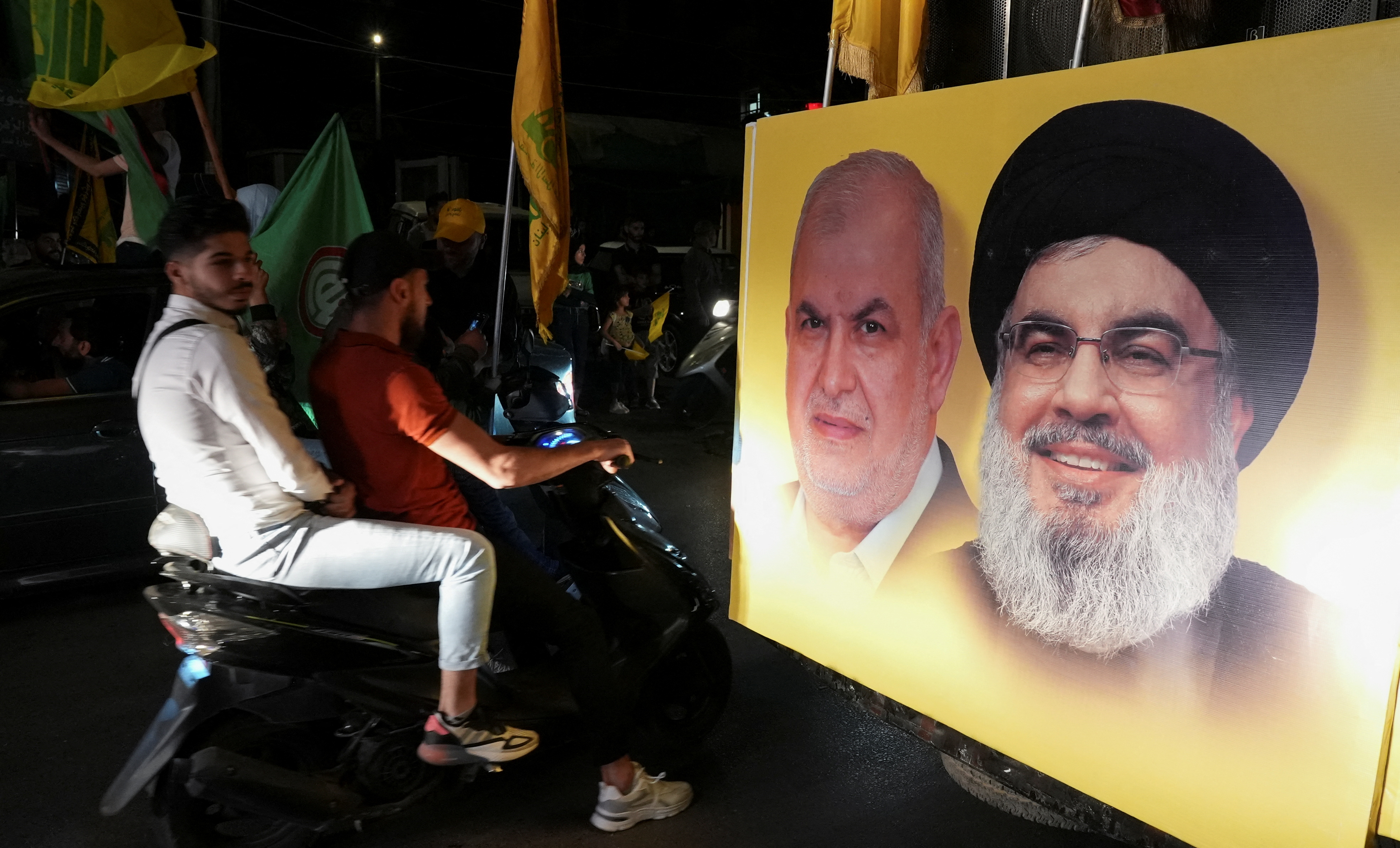 Supporters carry Hezbollah and Amal Movement flags as they ride in a convoy in Nabatiyeh