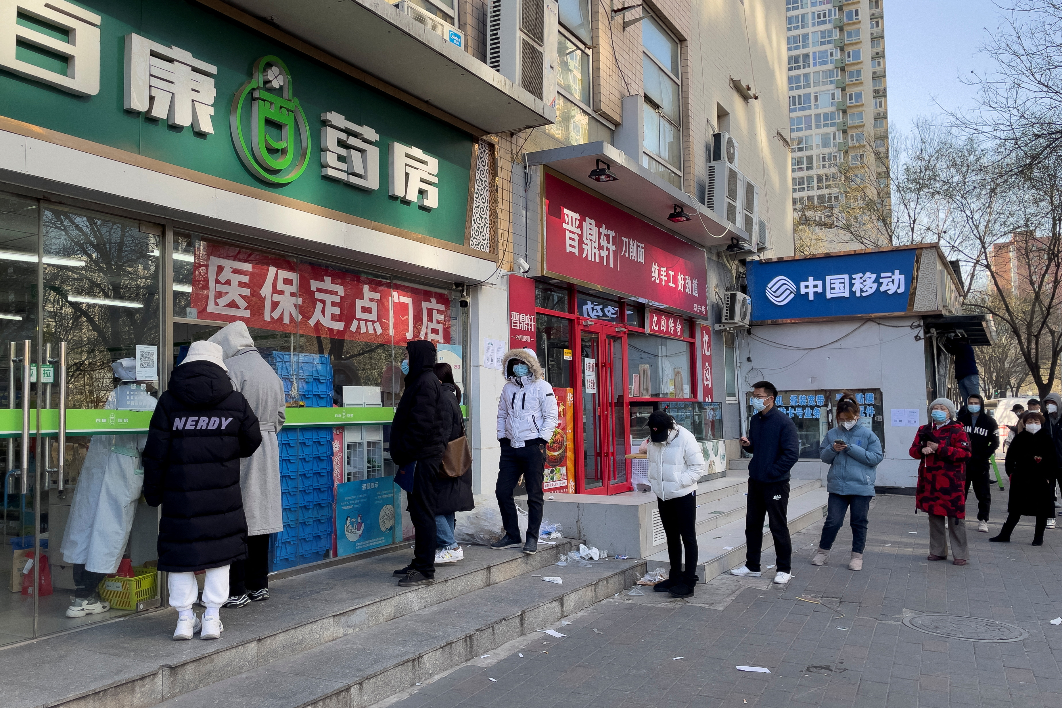 People wearing masks line up outside a pharmacy to buy products as coronavirus disease (COVID-19) outbreaks continue in Beijing
