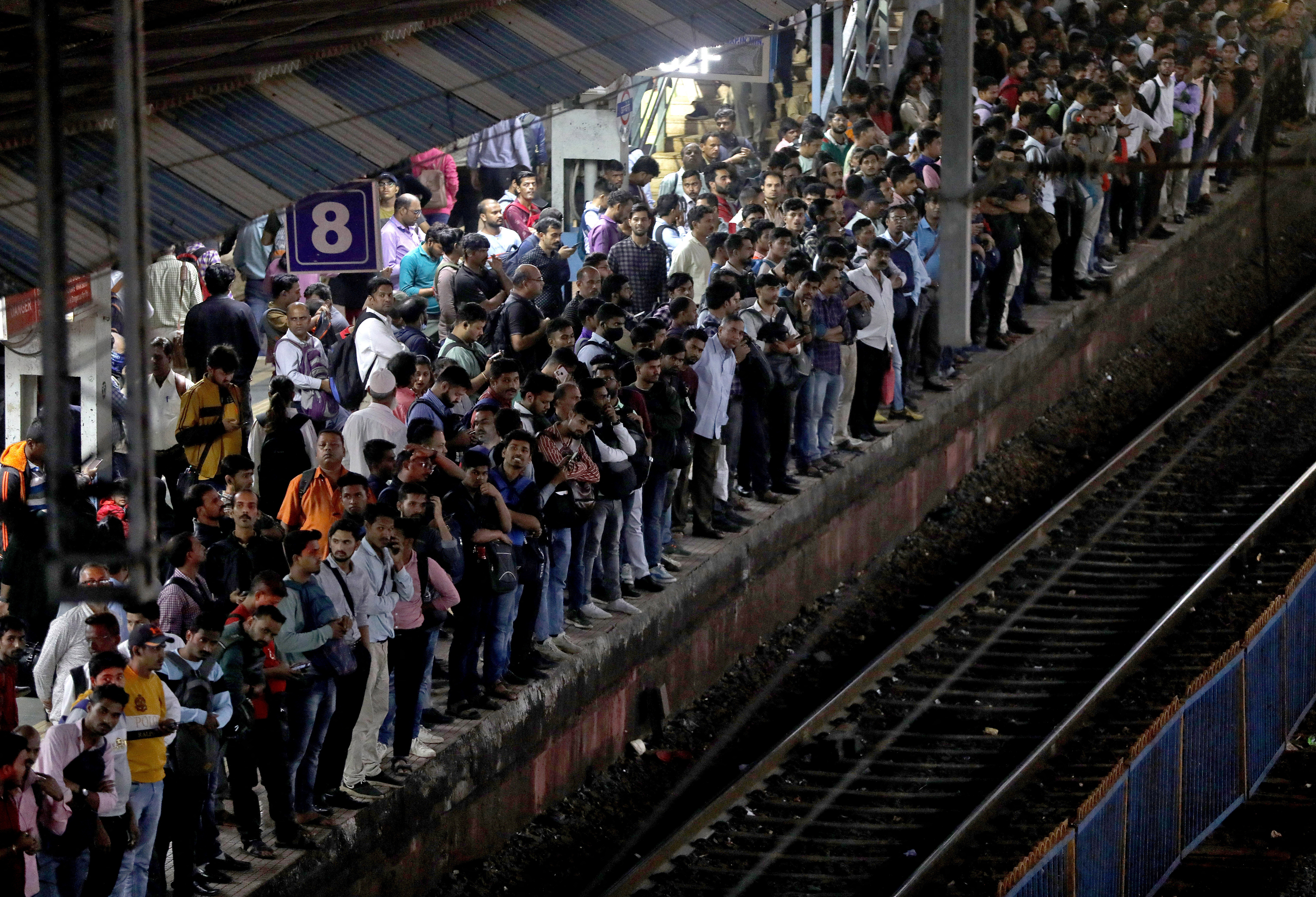 Commuters crowd on a platform as they wait to board suburban trains, in Mumbai