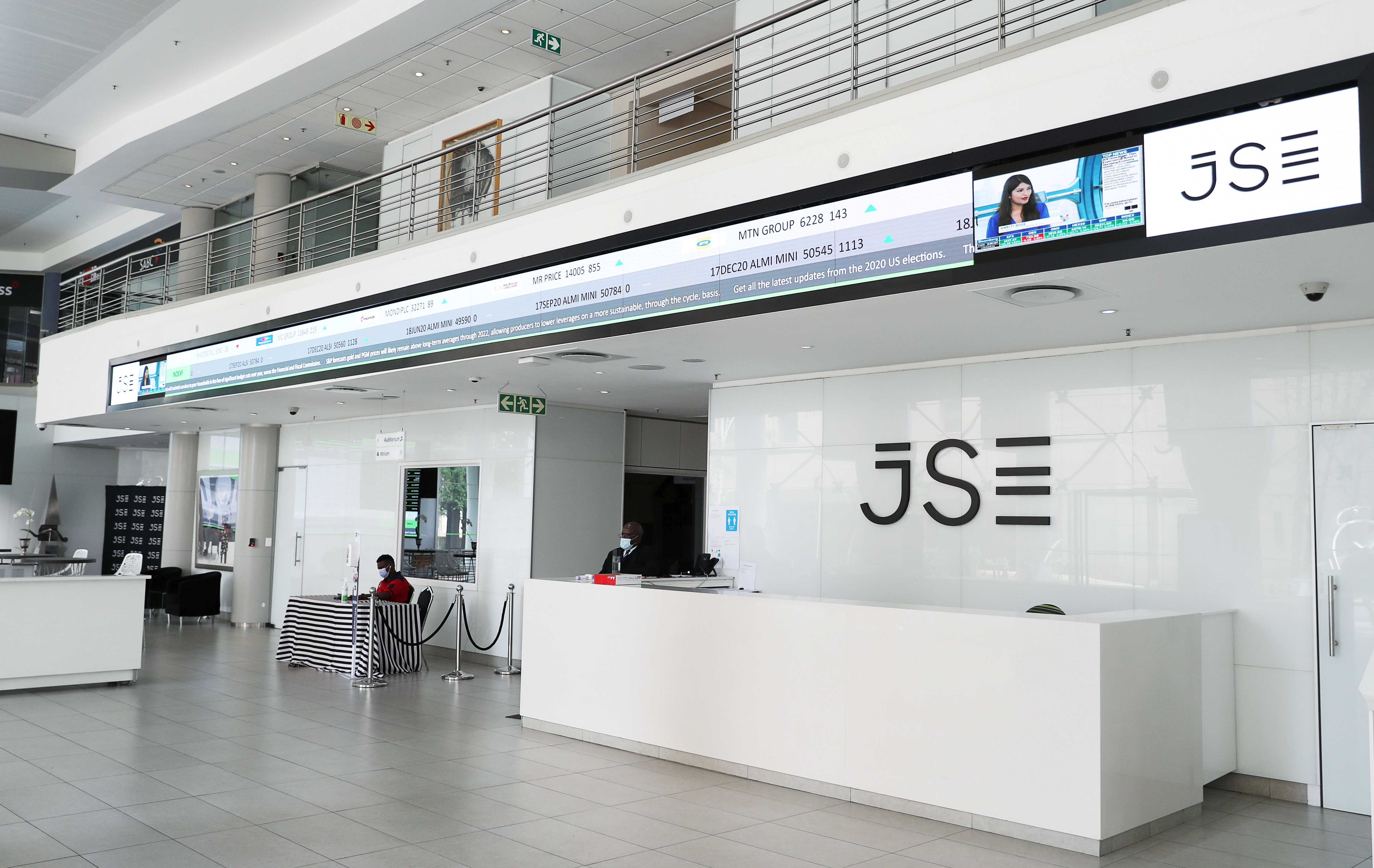 Workers wearing protective masks are seen at the reception with an electronic board displaying major indices at the Johannesburg Stock Exchange building in Sandton