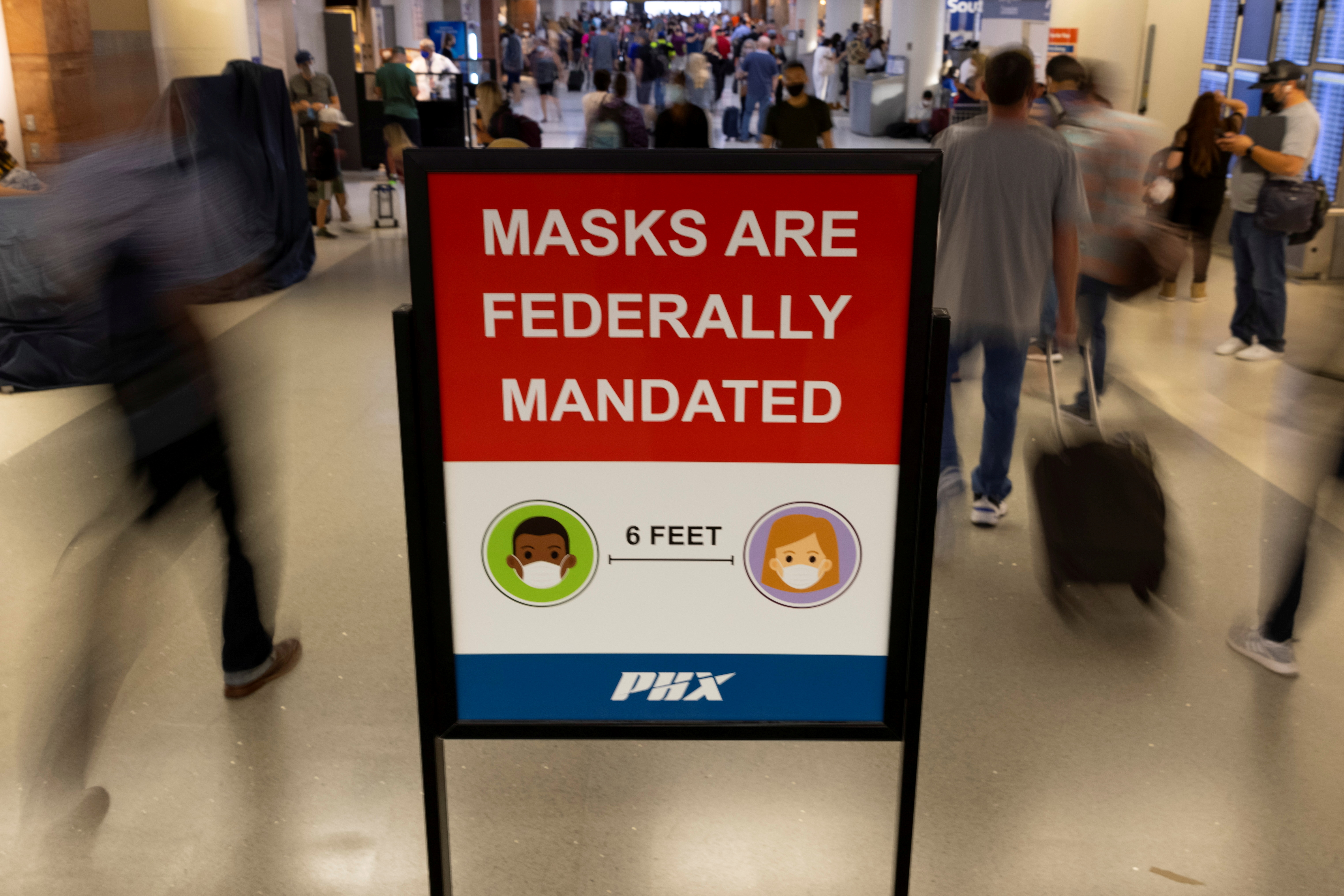 Air travelers make their way past a sign mandating face masks for all during the outbreak of the coronavirus disease (COVID-19) in Phoenix