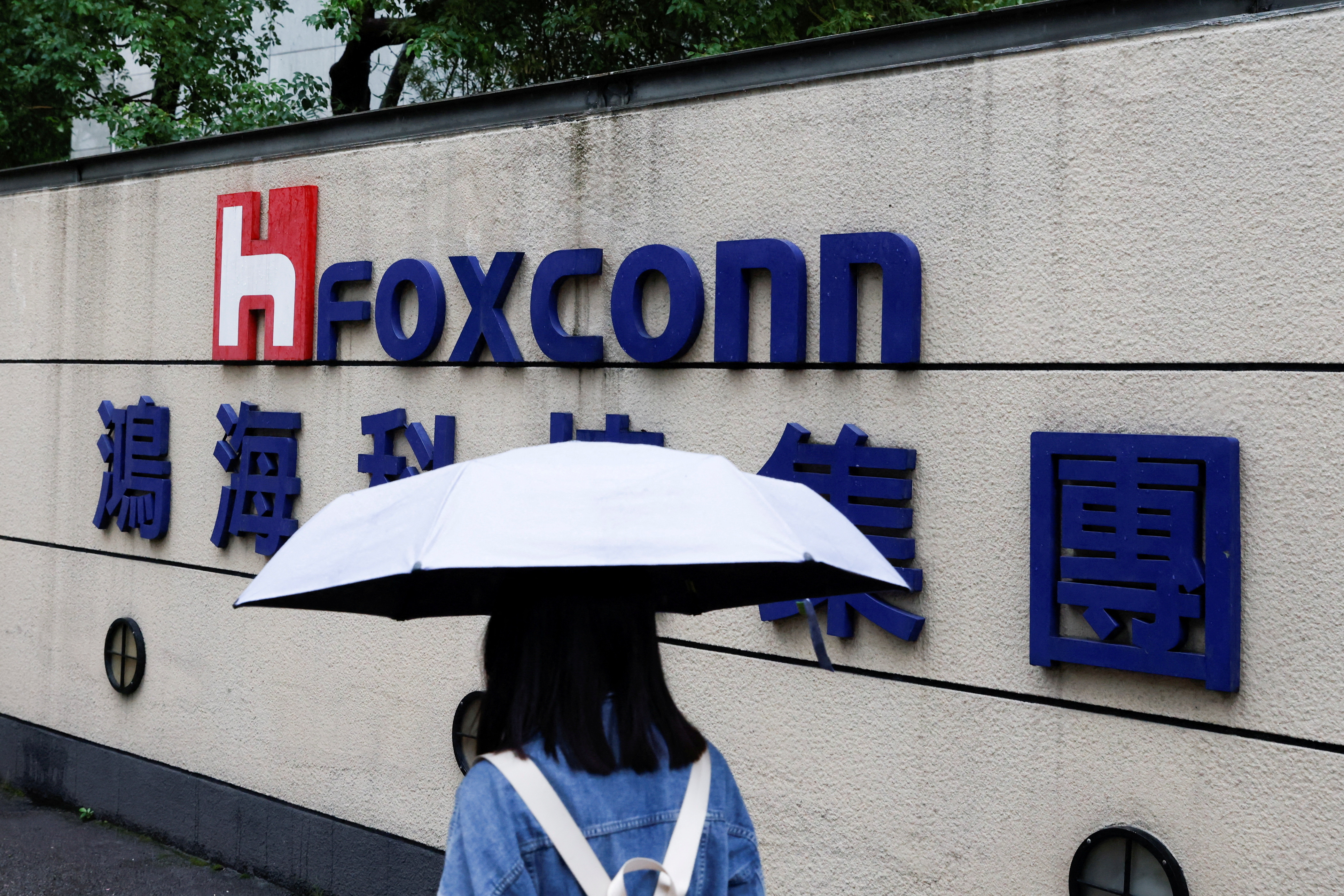 A woman carrying an umbrella walks past the logo of Foxconn outside a company's building in Taipei