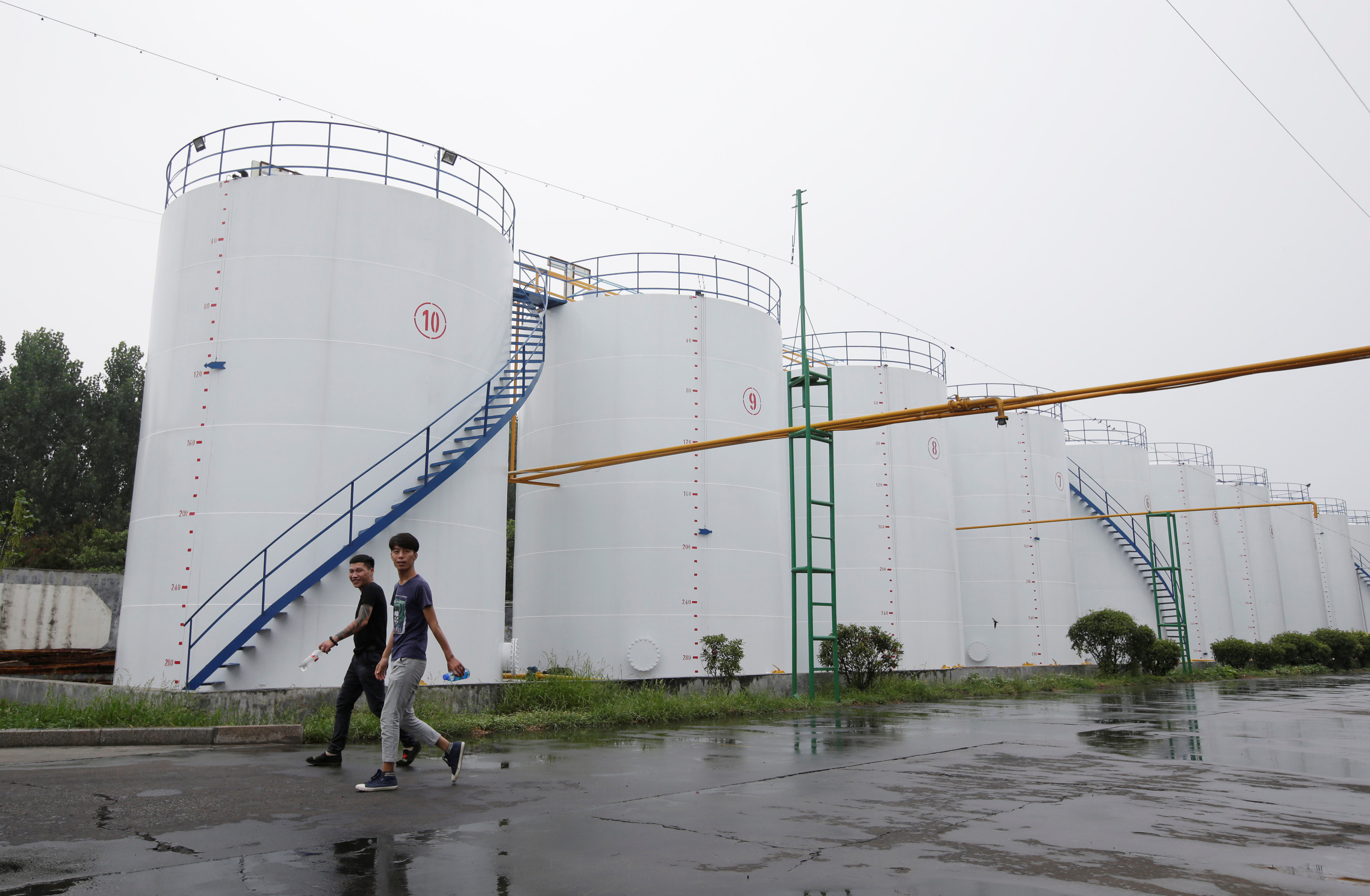 Men walk past oil tanks at the plant of Liangyou Industry and Trade Co., Ltd in Qufu