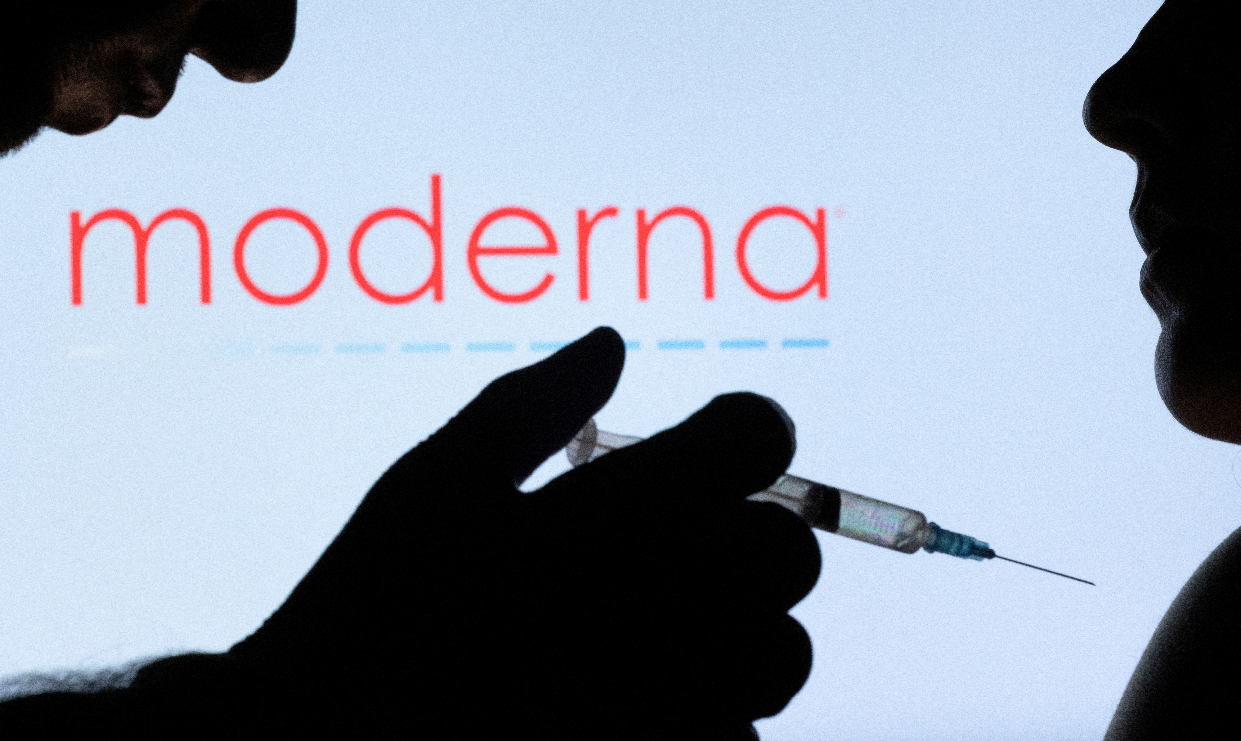 People pose with a syringe and needle in front of a displayed Moderna logo