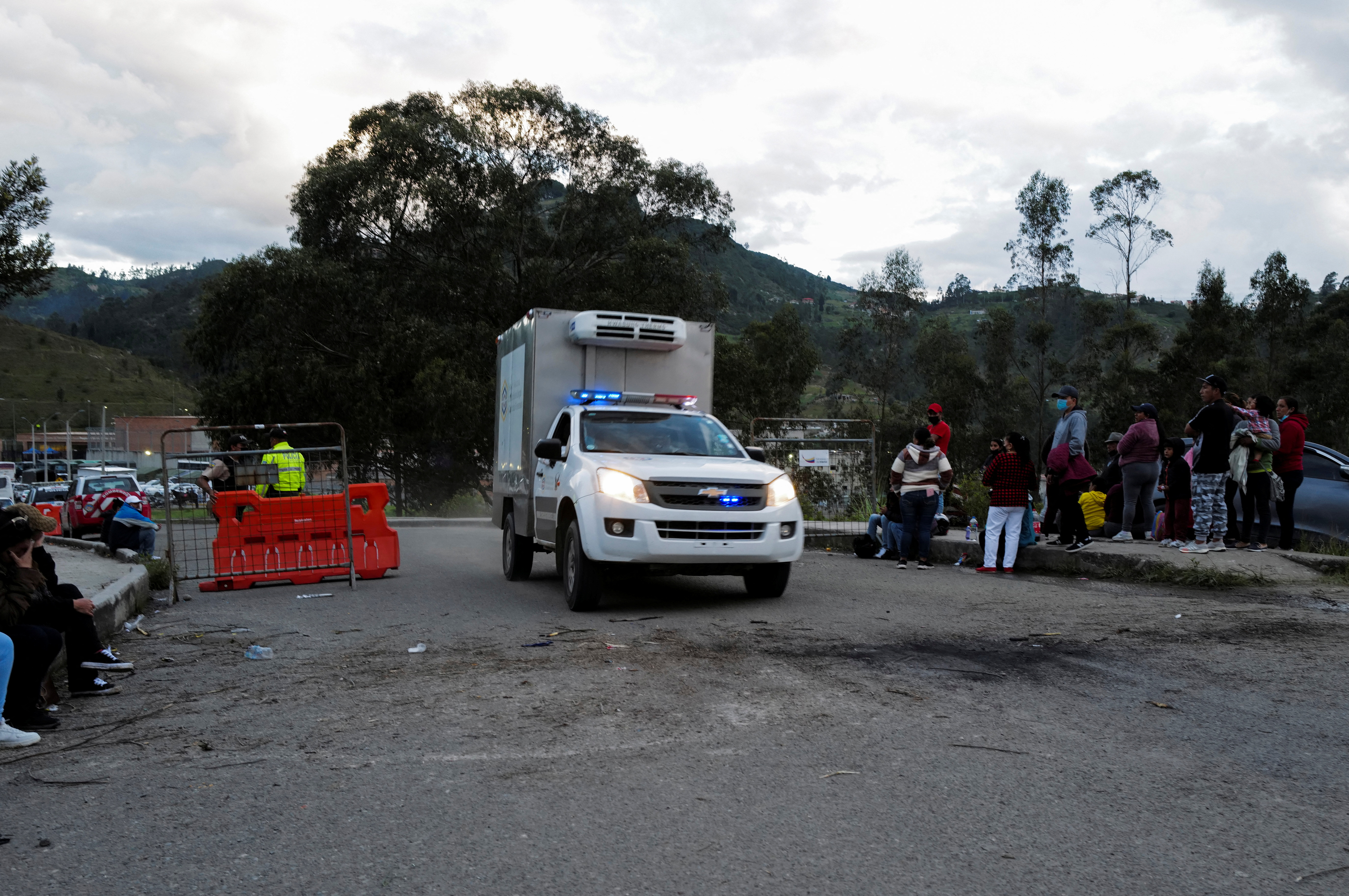 A medical vehicle carrying dead bodies drives past a police checkpoint where relatives of inmates wait for news of their loved ones after a riot broke out at the El Turi prison where several inmates were killed or injured, in Cuenca