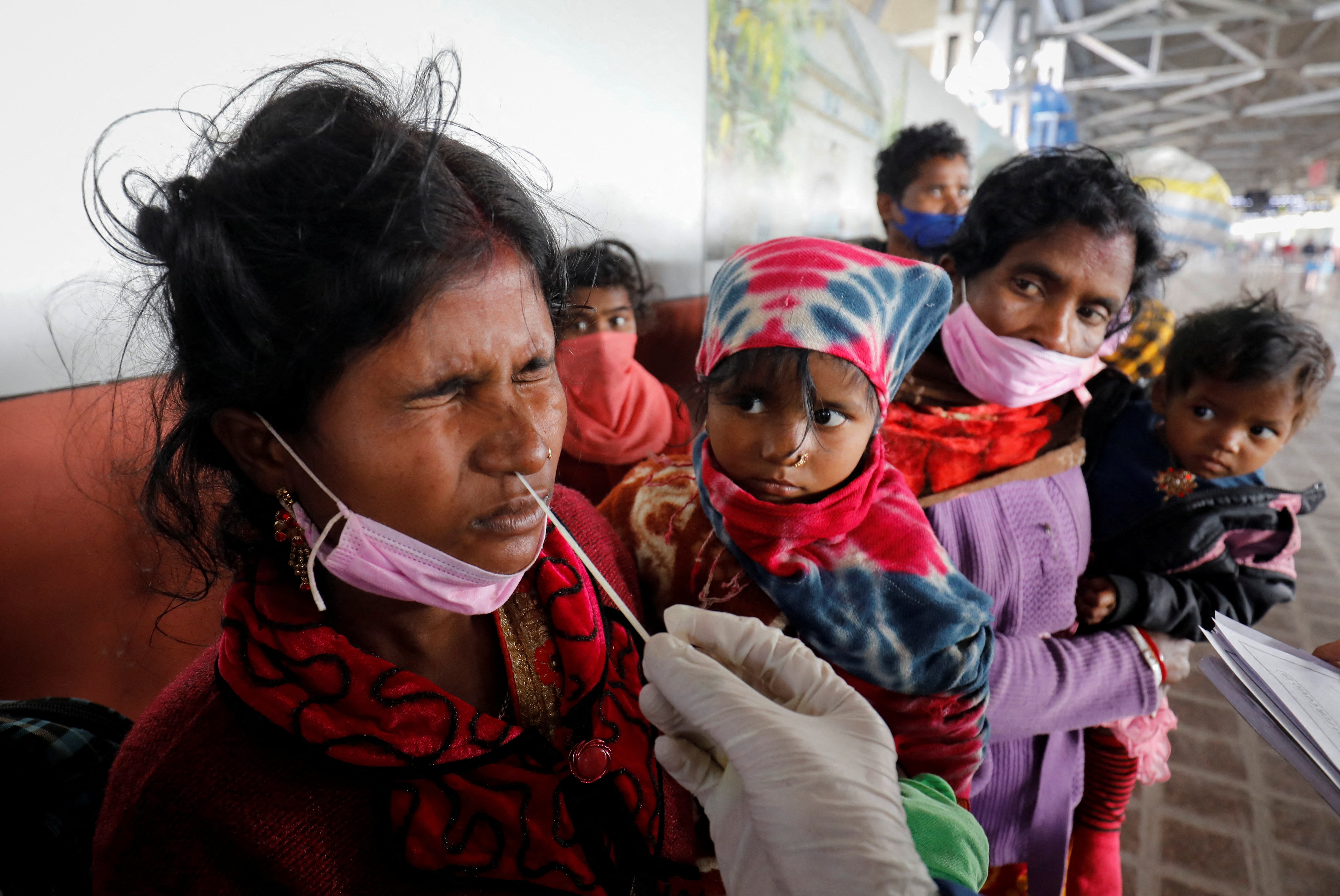A woman reacts as a healthcare worker collects a swab sample from her to test for the coronavirus disease (COVID-19) at a railway station in Ahmedabad
