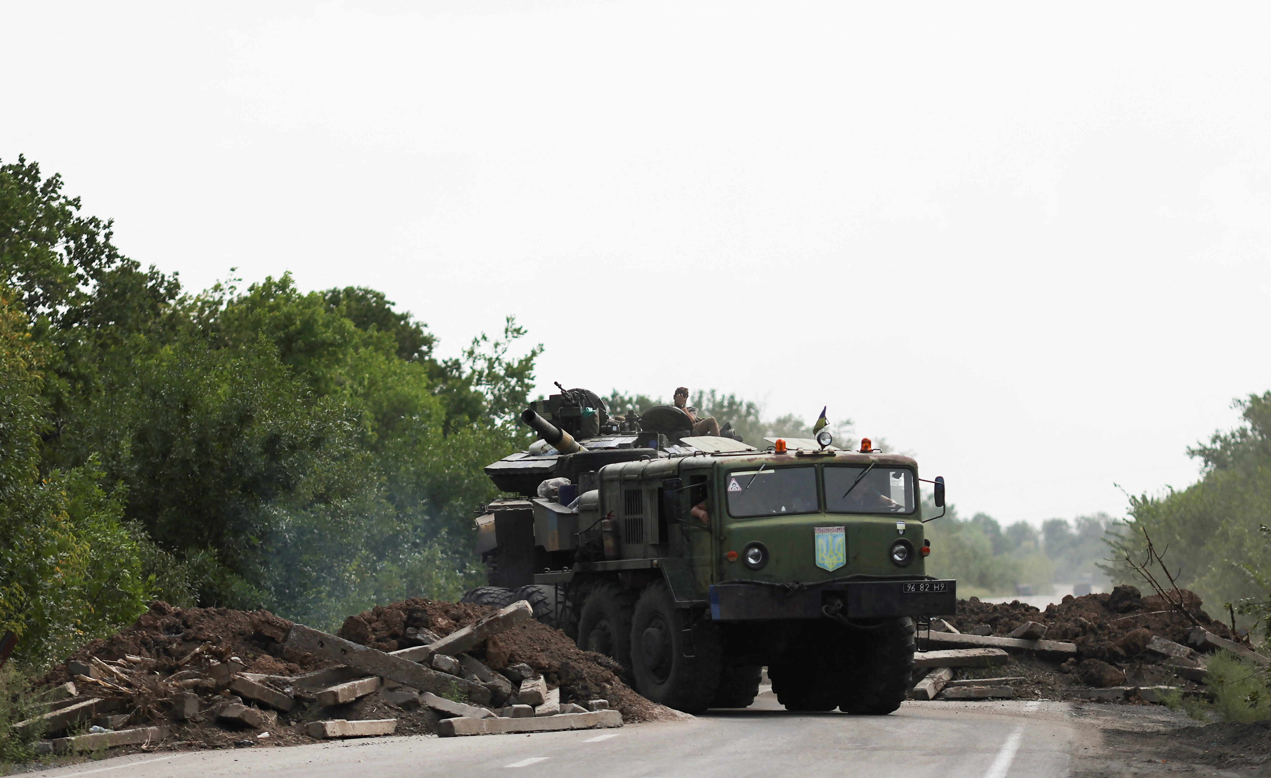 A Ukrainian serviceman gestures on a tank, as it is towed away by a military truck near Bakhmut