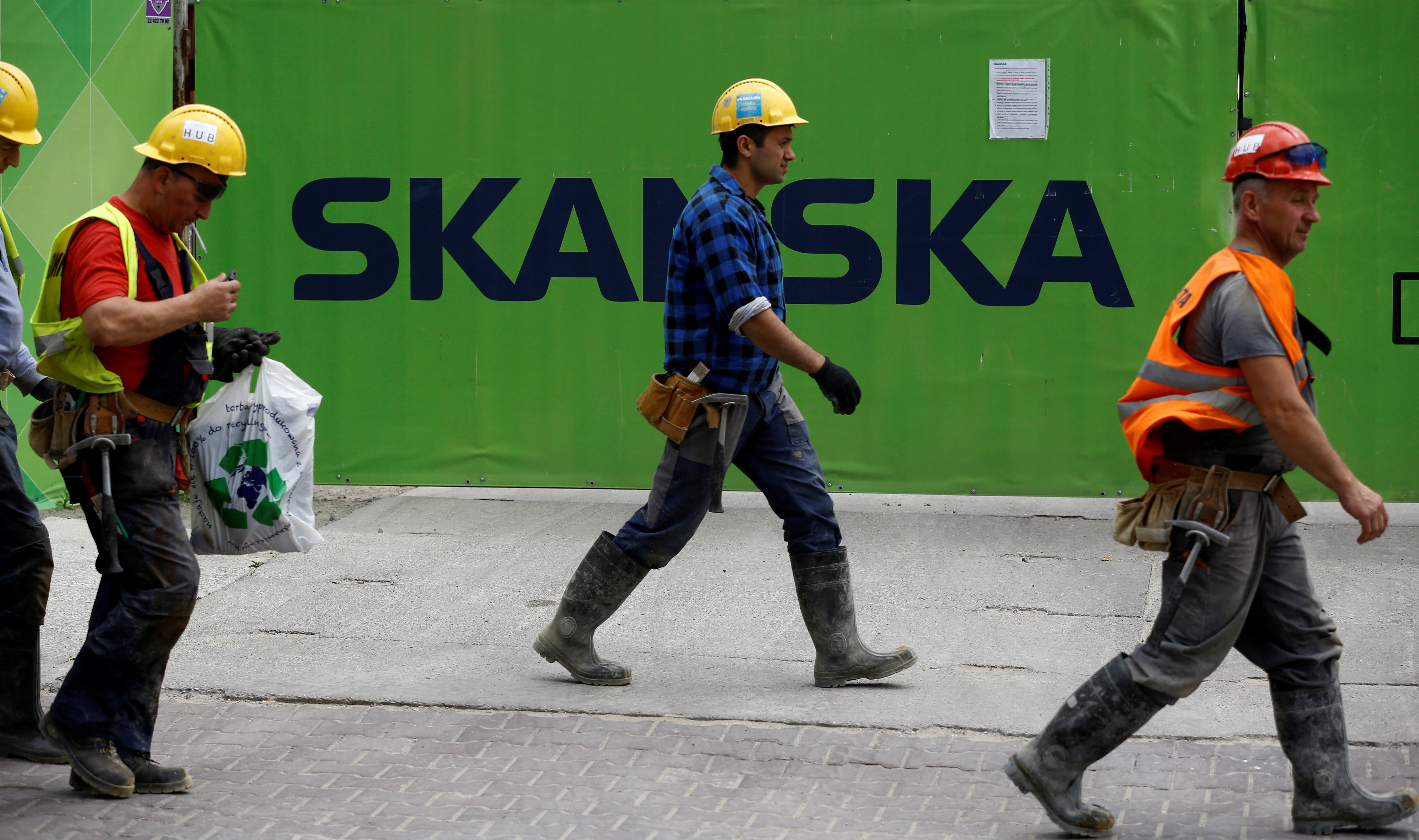 Workers walk past a Skanska logo seen on a fence at a construction site In Warsaw, Poland