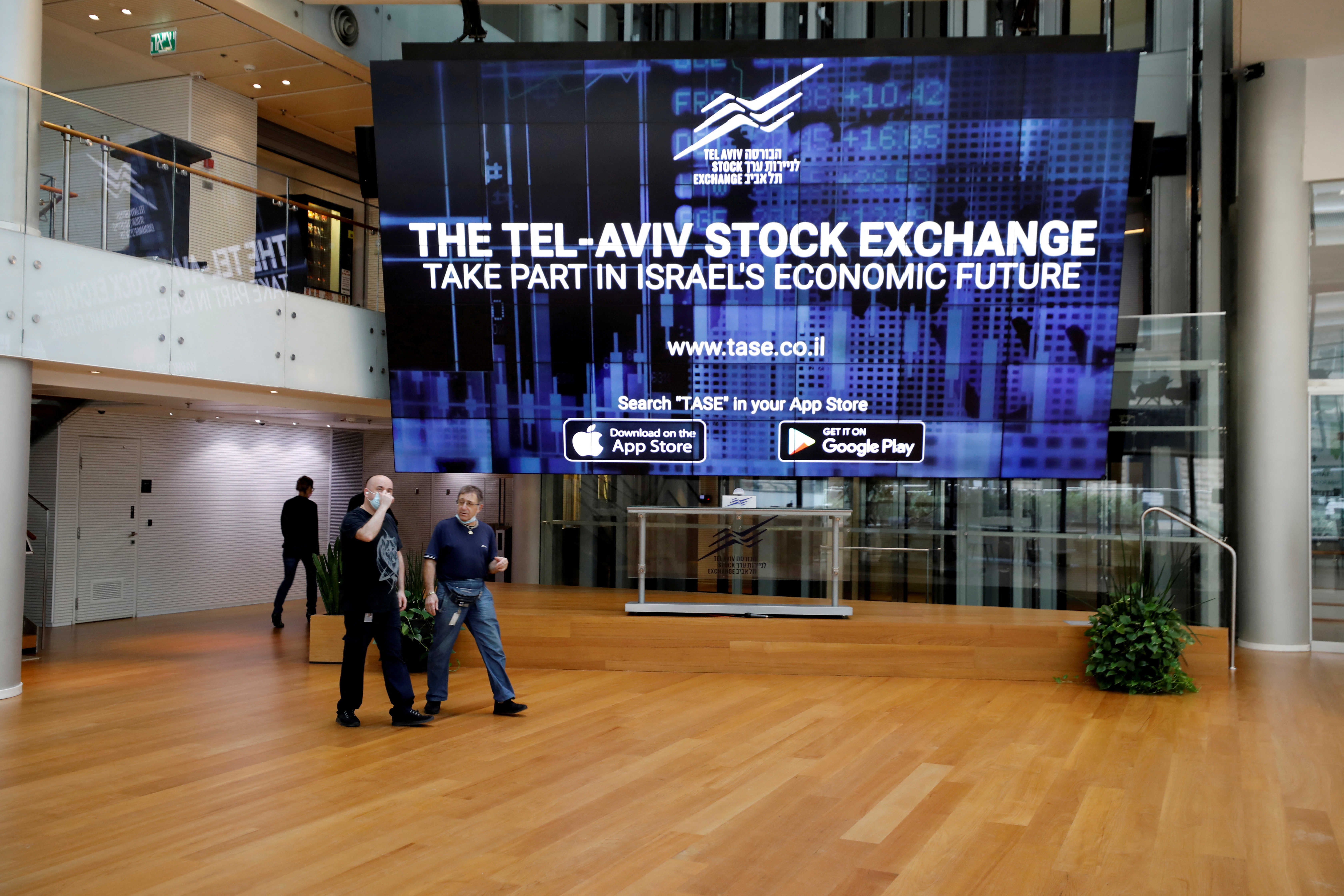 Men walk past an electronic board at the Tel Aviv Stock Exchange in Tel Aviv