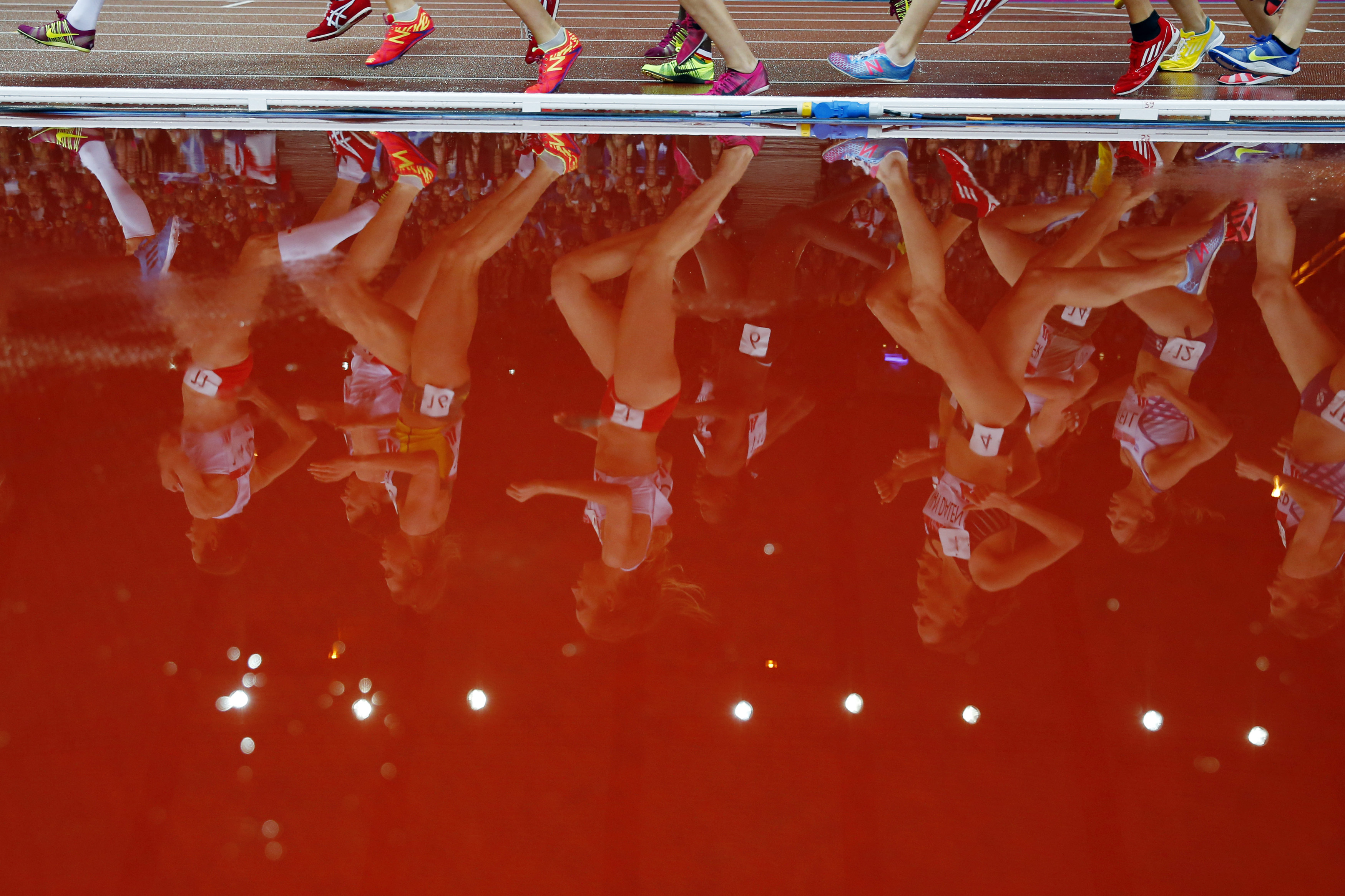 Runners are reflected in a puddle as they compete in the women's 5000m race at the 2014 Commonwealth Games in Glasgow