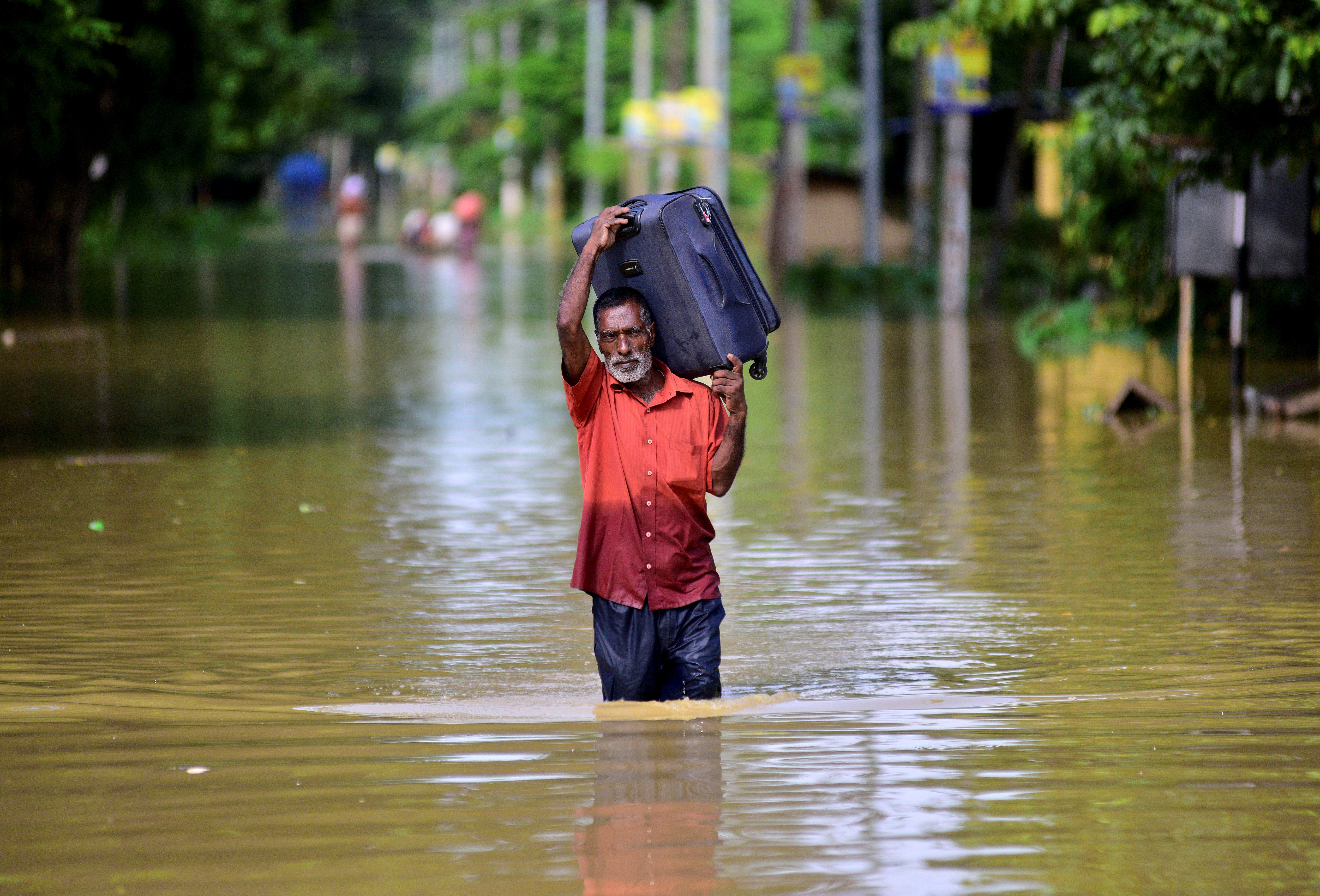 A flood-affected man carrying a luggage wades through a flooded road as he moves to a safer place after heavy rains in Nagaon district