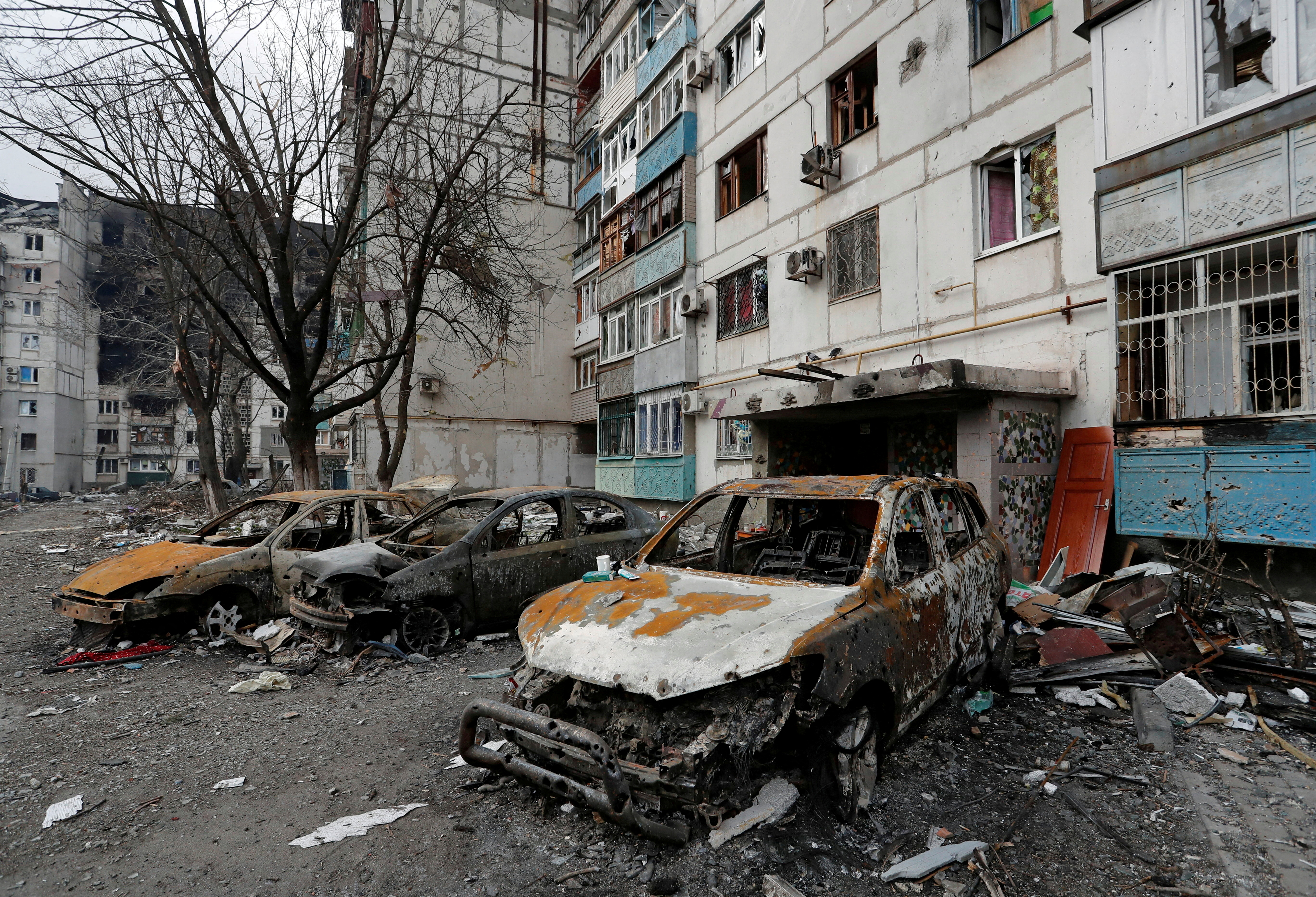Destroyed cars are seen in front of a damaged apartment building in the besieged city of Mariupol