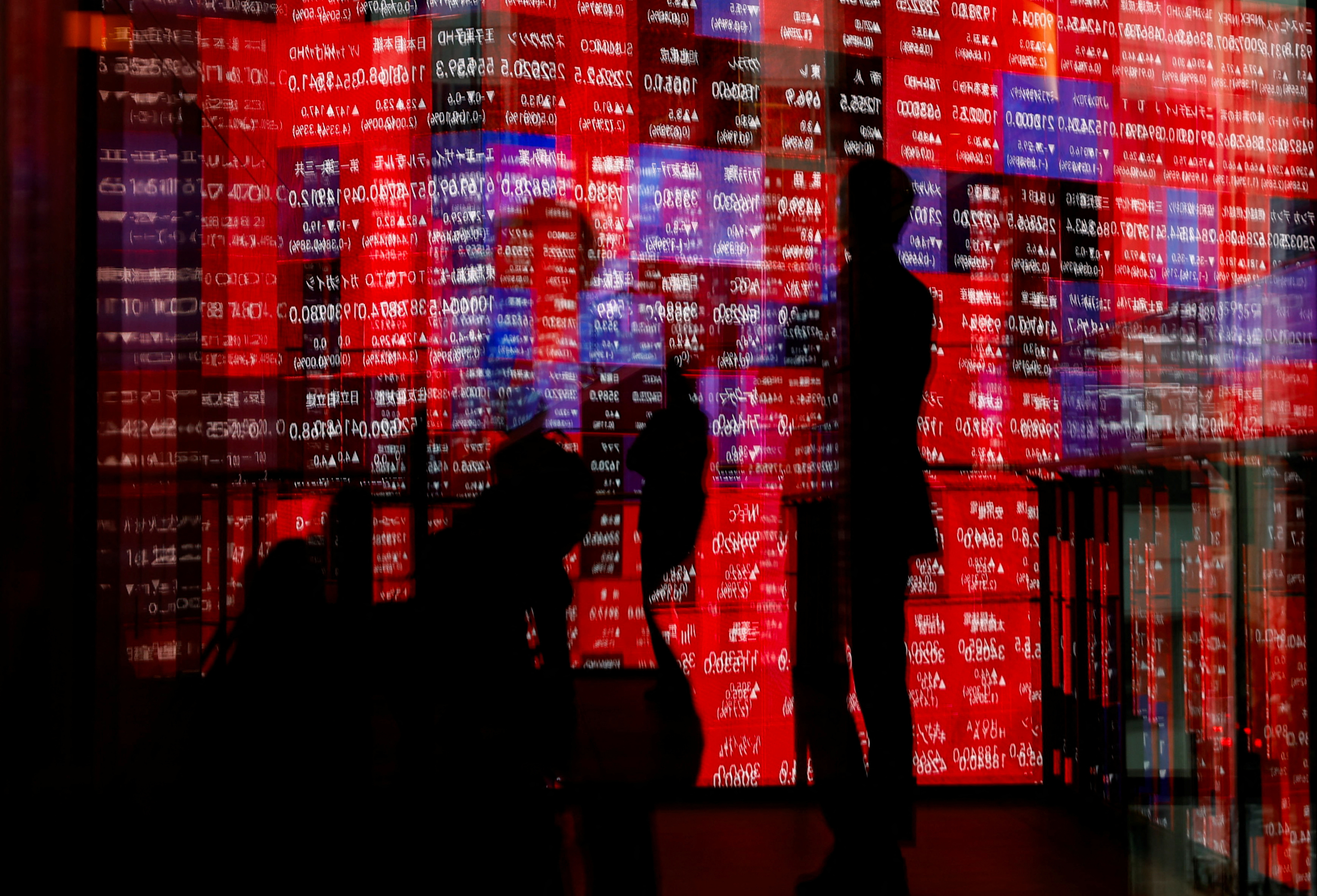 Visitors and electronic screens displaying Japan's Nikkei stock quotation board are reflected on window glasses in Tokyo