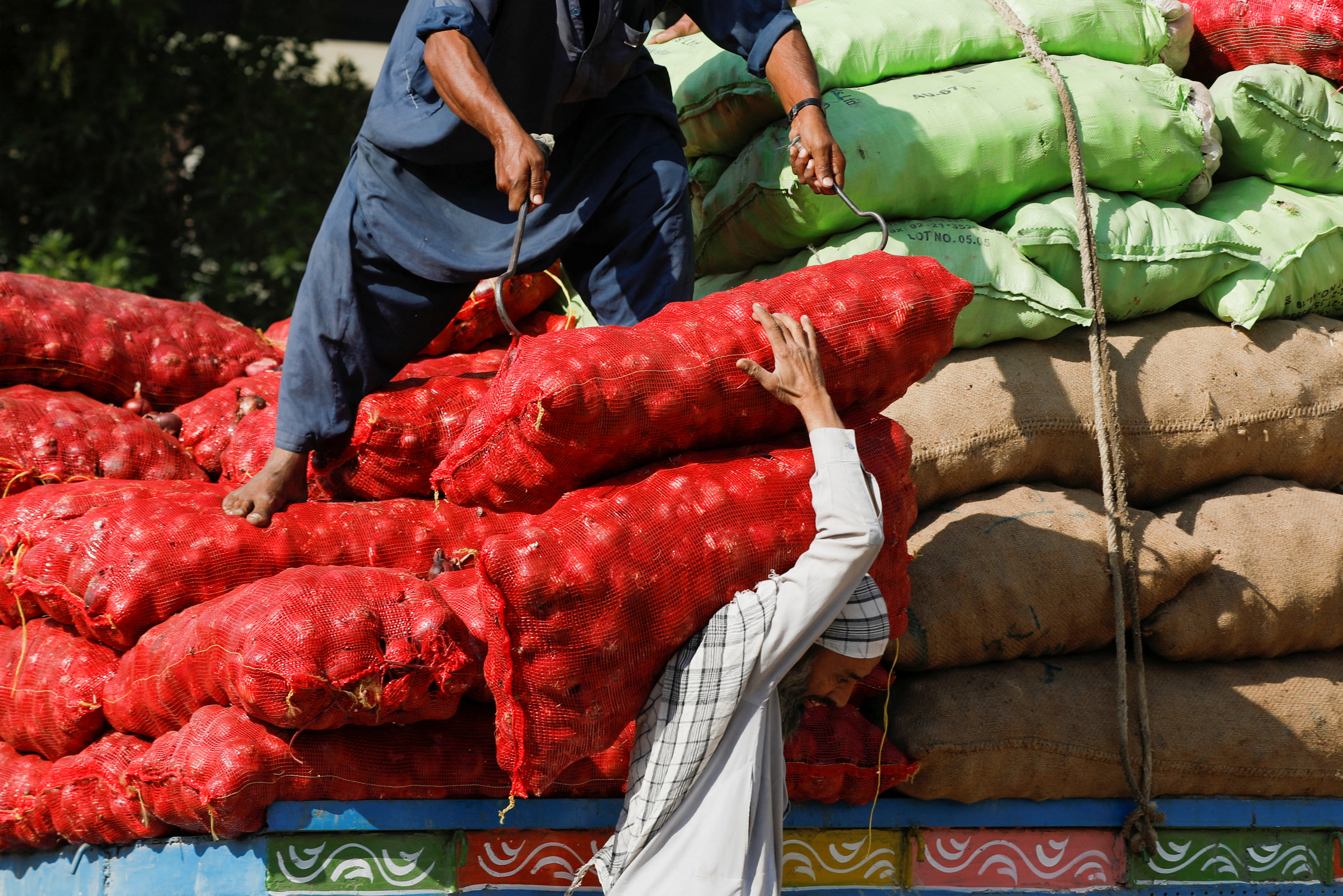 Labourers unload sacks of onion from a truck to supply at a market in Karachi