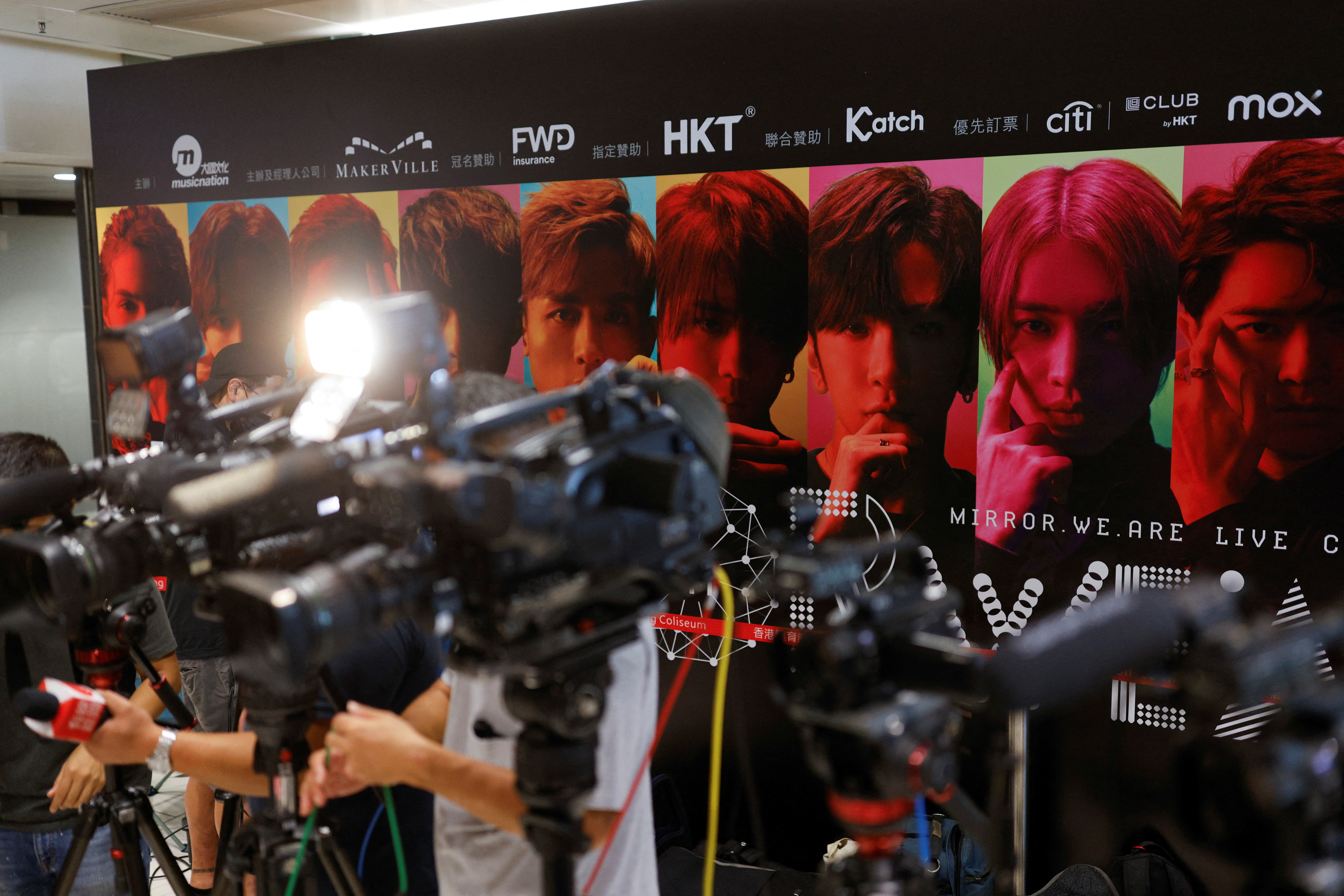 Members of the media are seen in front of a background showing Hong Kong boyband Mirror during a news conference after a giant video panel fell onto the stage during a concert, in Hong Kong