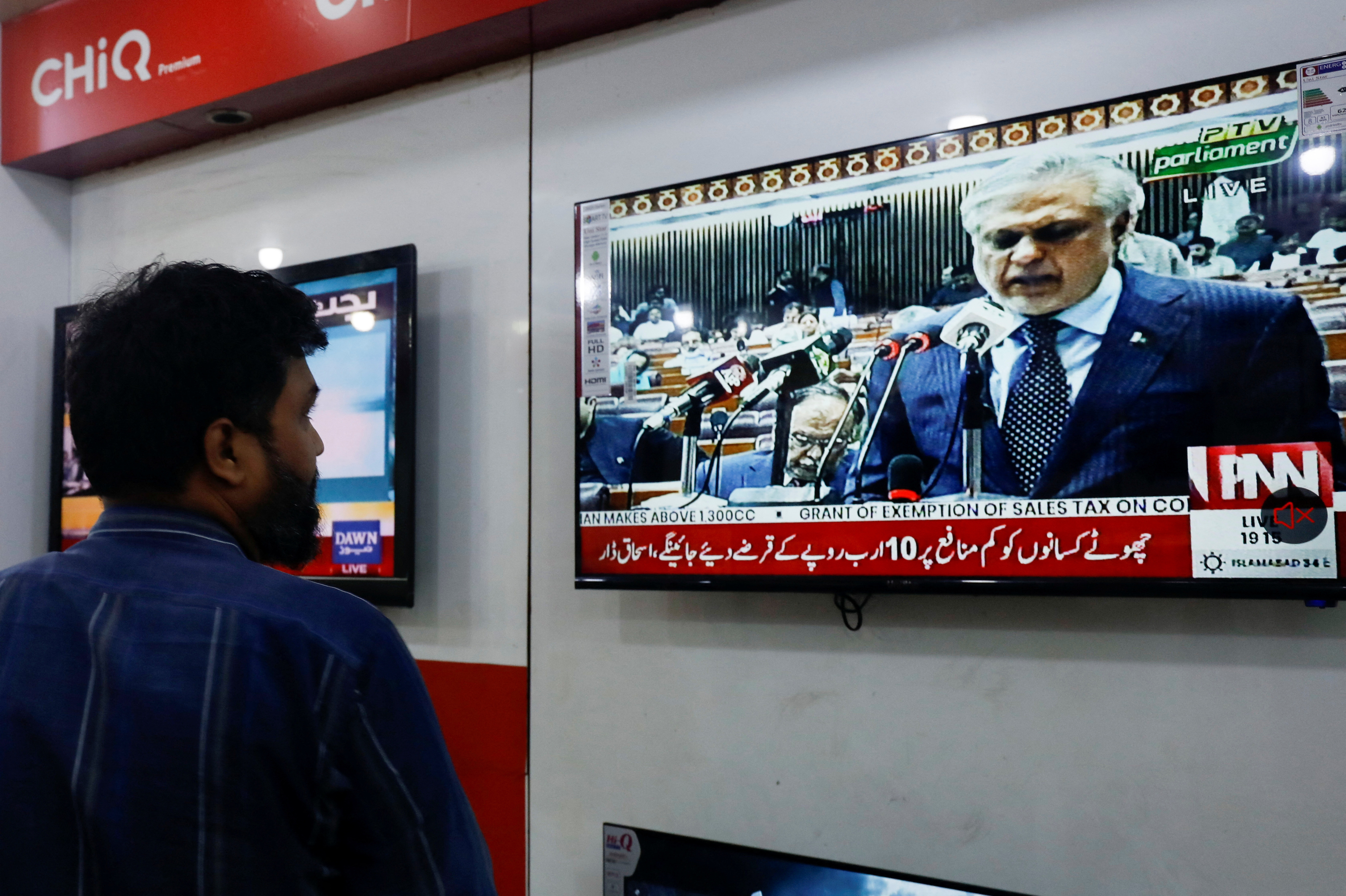 A salesman looks at a television screen showing the Pakistan's Finance Minister Ishaq Dar presenting the budget for the 2023/24 fiscal year, at a shop in Karachi