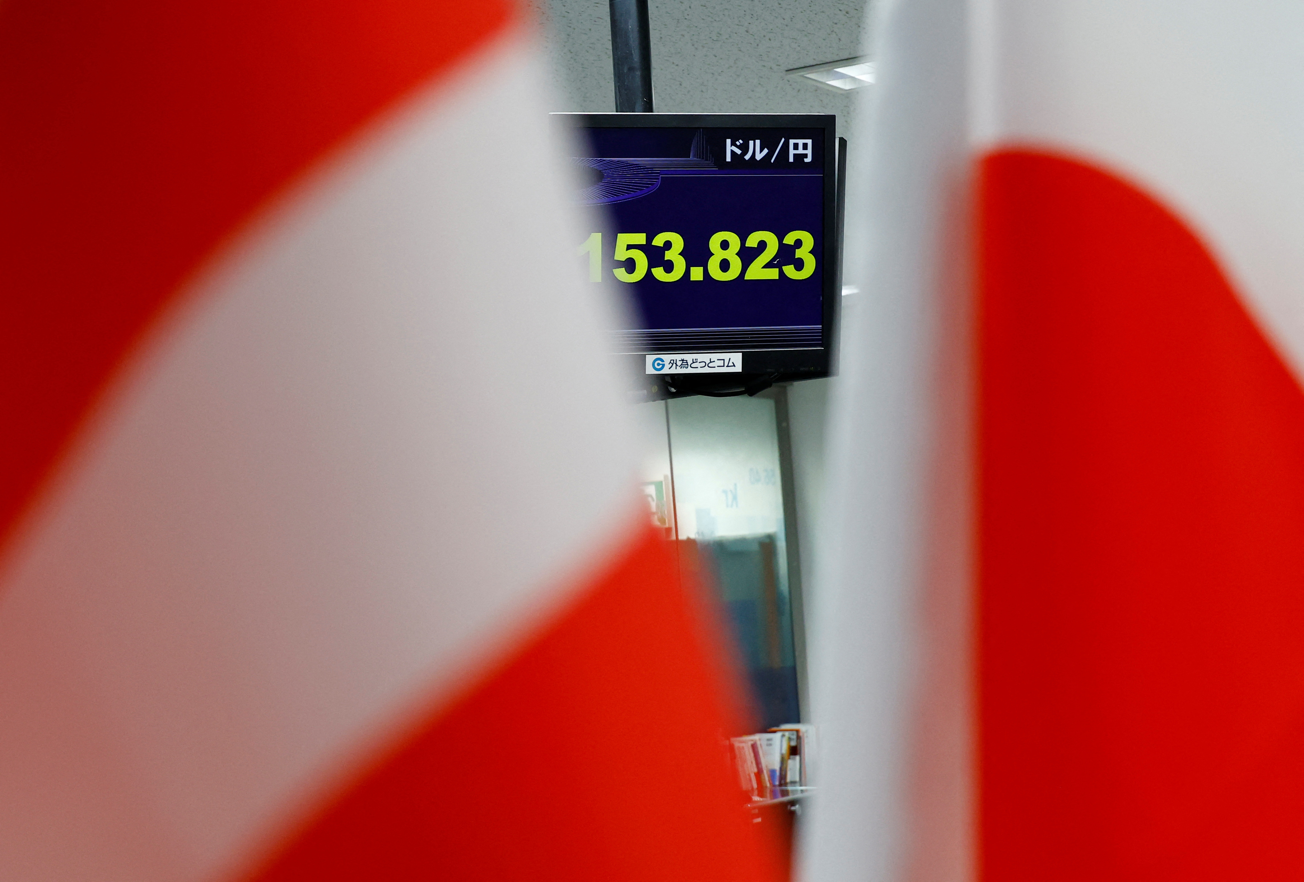 A monitor displaying the Japanese yen exchange rate against the U.S. dollar is seen between the national flags of the U.S and Japan at a dealing room of he foreign exchange trading company Gaitame.com in Tokyo