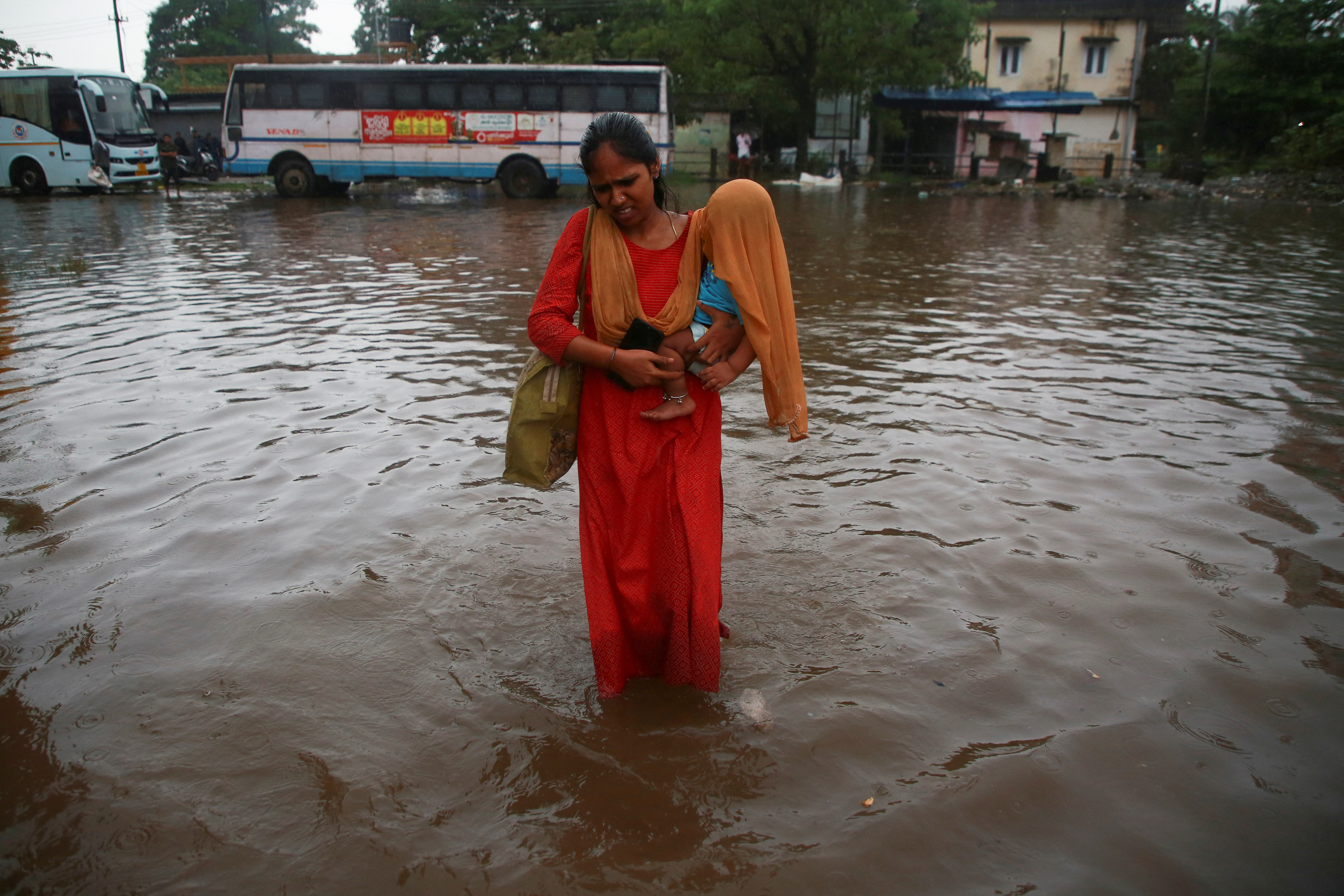 A woman carries her son, covered with a scarf, through a water-logged bus terminal as it rains in Kochi