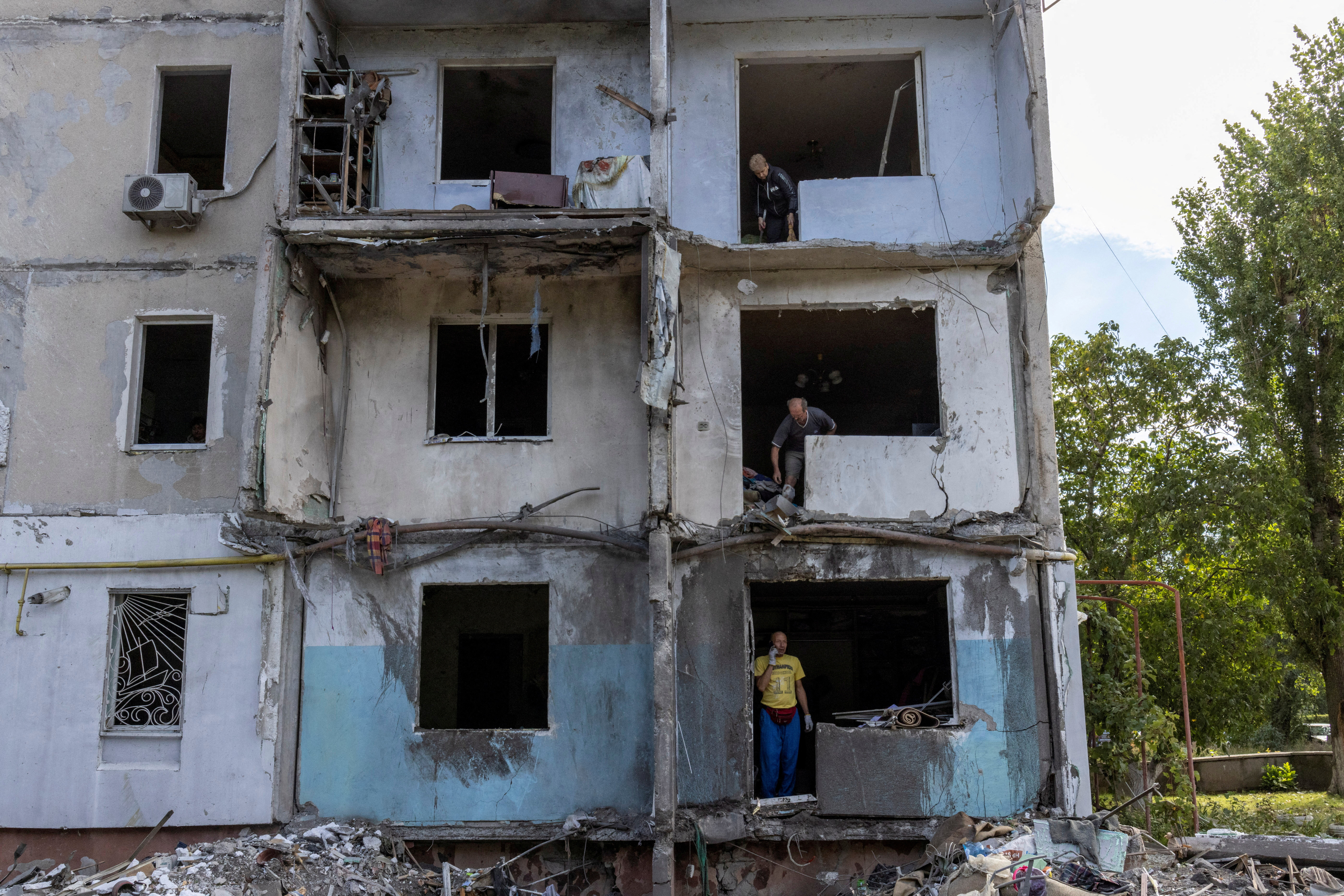 People stand, inspect and clean their apartments at a residential building destroyed by a strike in Mykolaiv