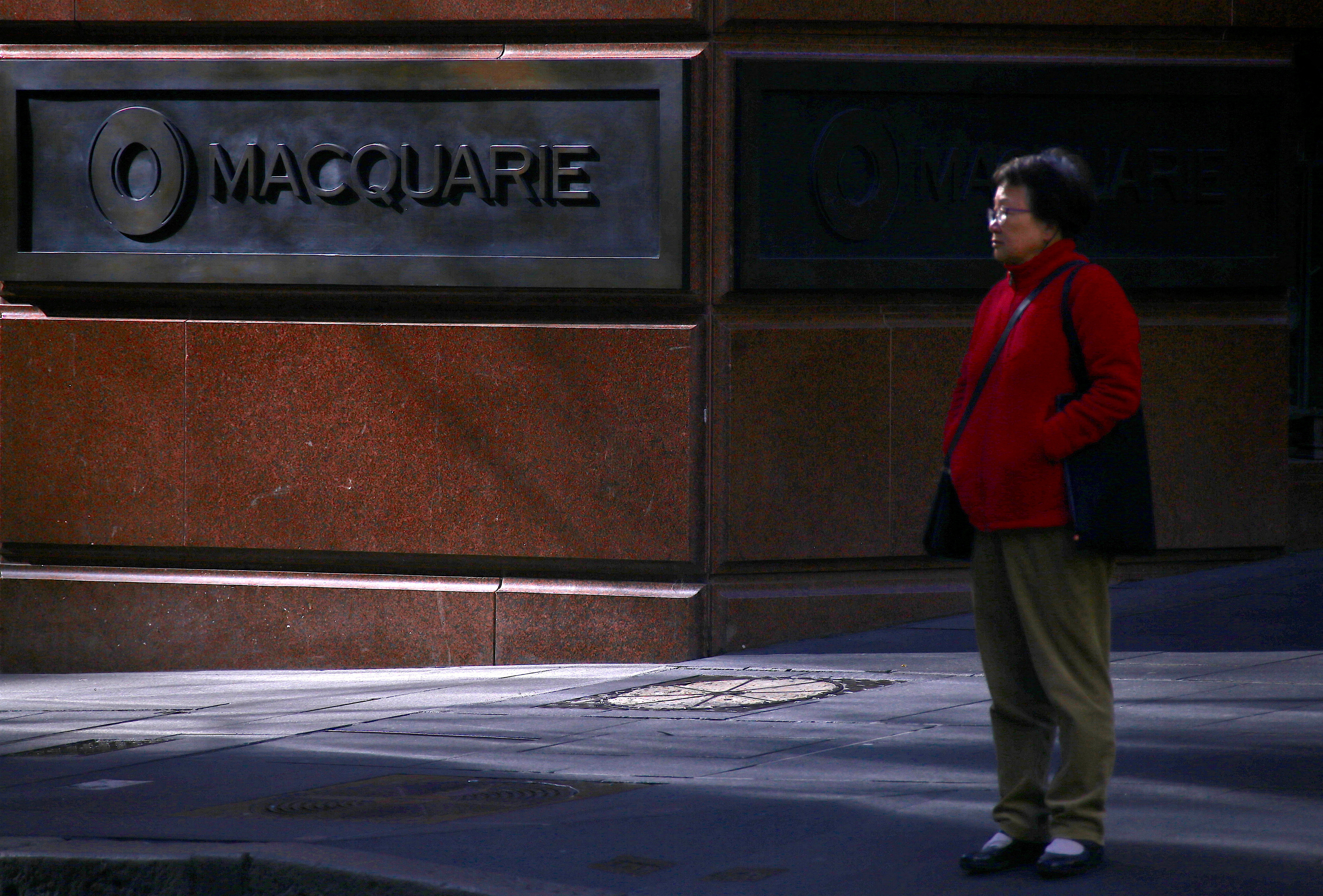 A pedestrian stands near the logo of Australia's biggest investment bank Macquarie Group Ltd which adorns a wall on the outside of their Sydney office headquarters in central Sydney, Australia