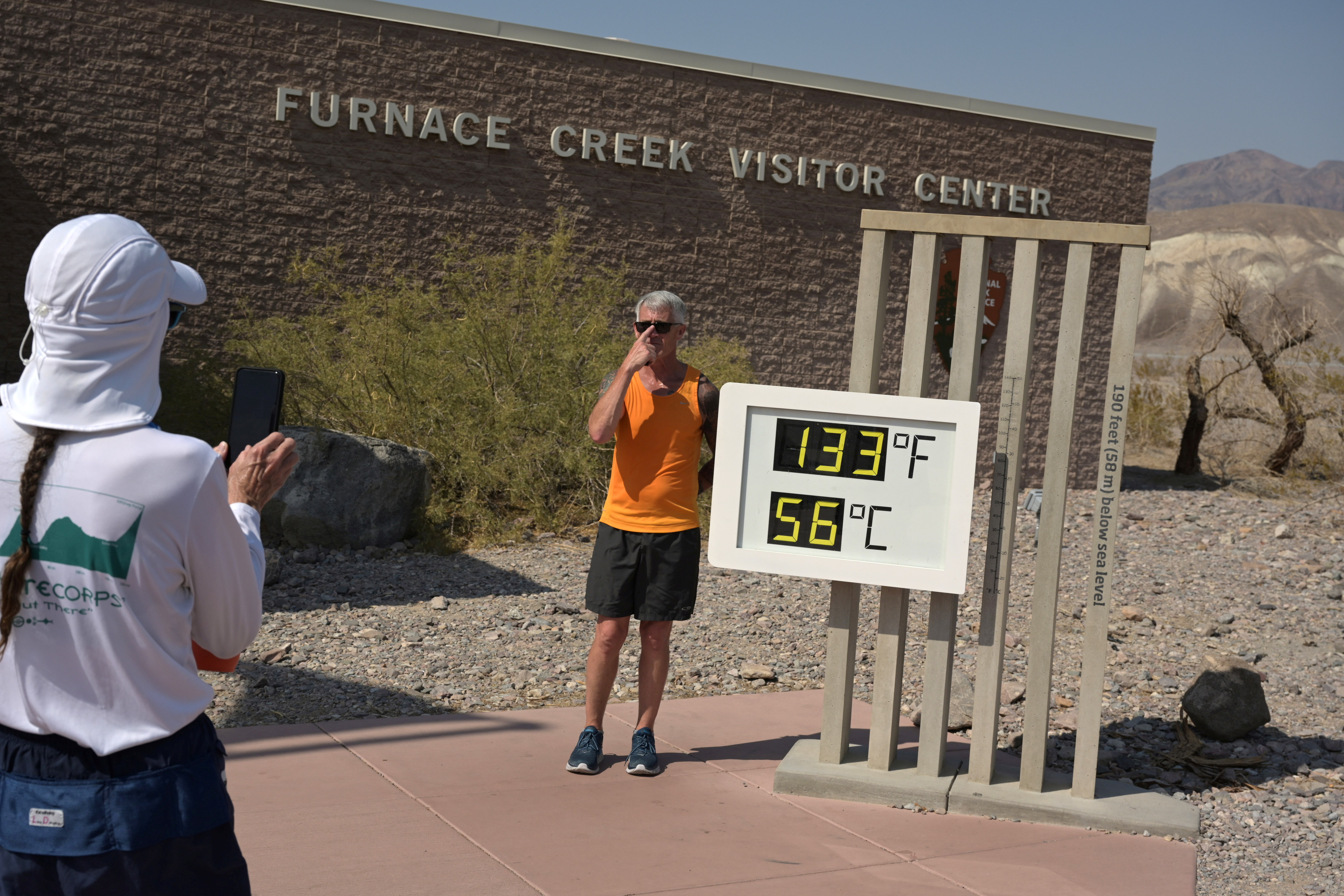 A person poses for a photo next to a thermometer in Death Valley
