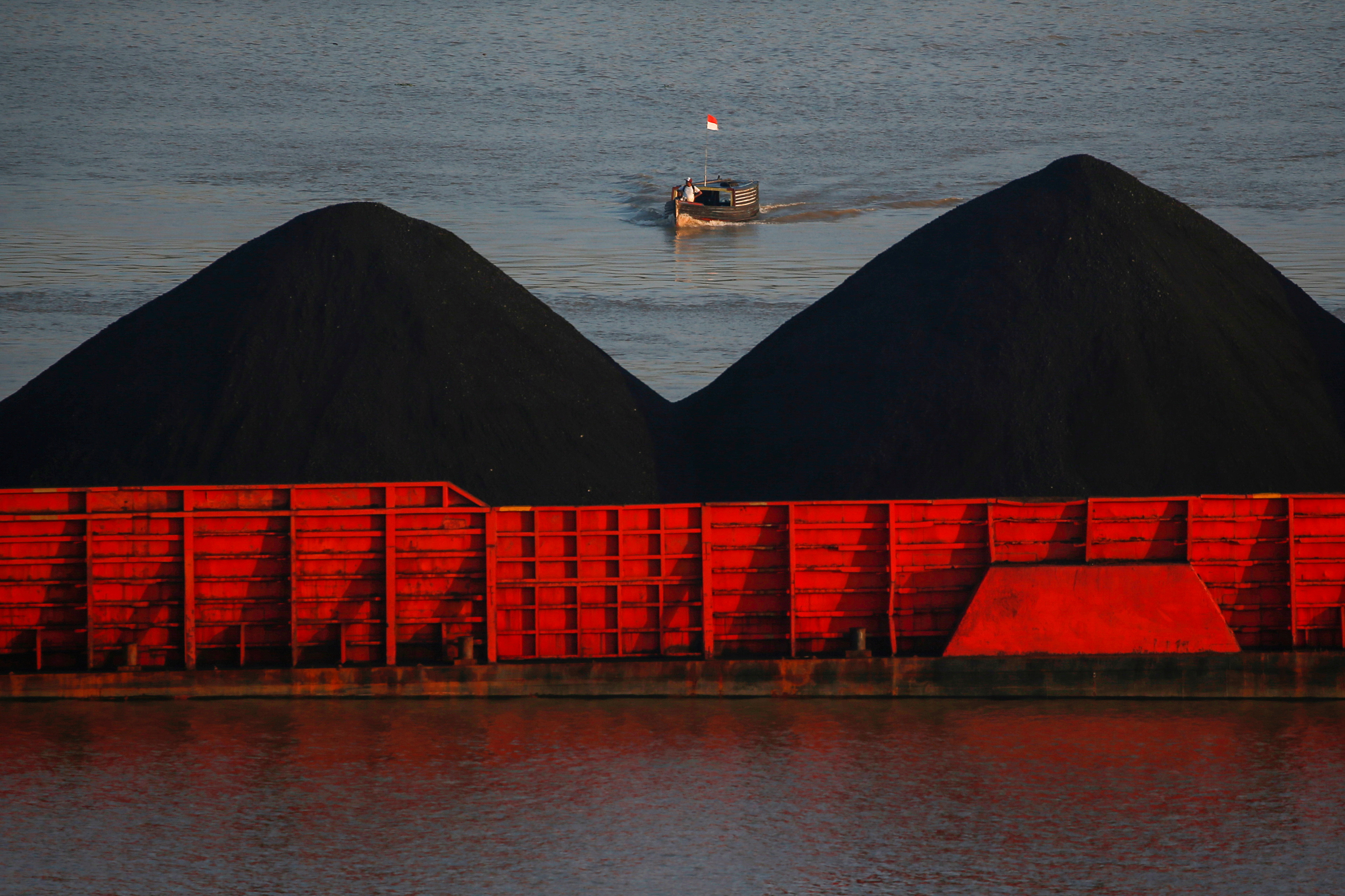 Man stands on a boat as coal barges queue to be pull along Mahakam river in Samarinda