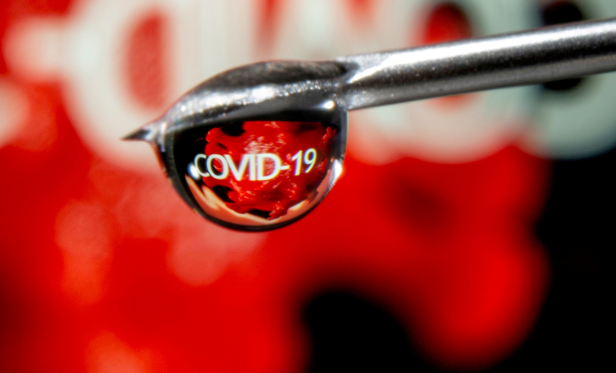 The word "COVID-19" is reflected in a drop on a syringe needle in this illustration
