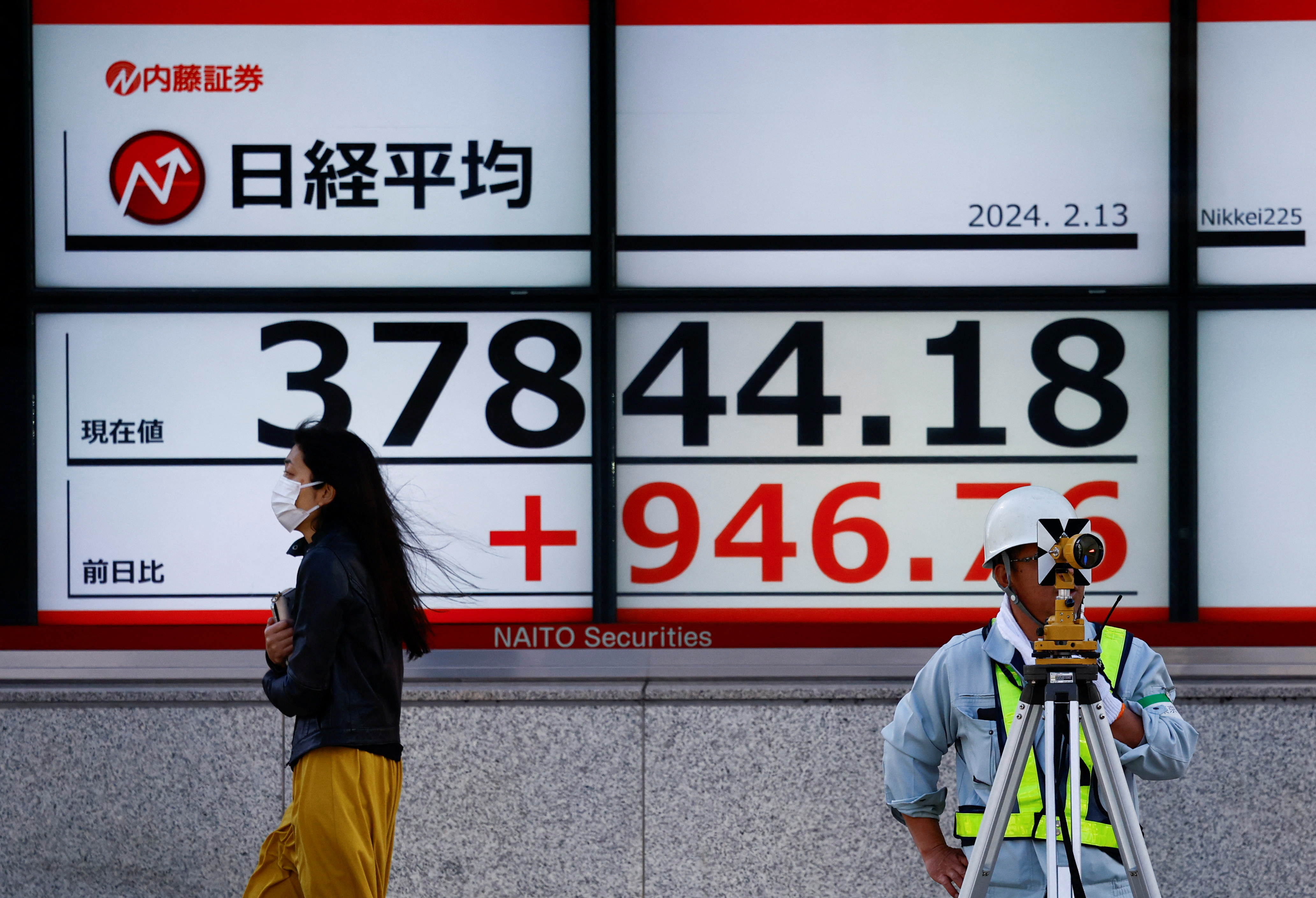 Passersby walk past in front of an electric screen displaying Japan's Nikkei share average outside a brokerage in Tokyo