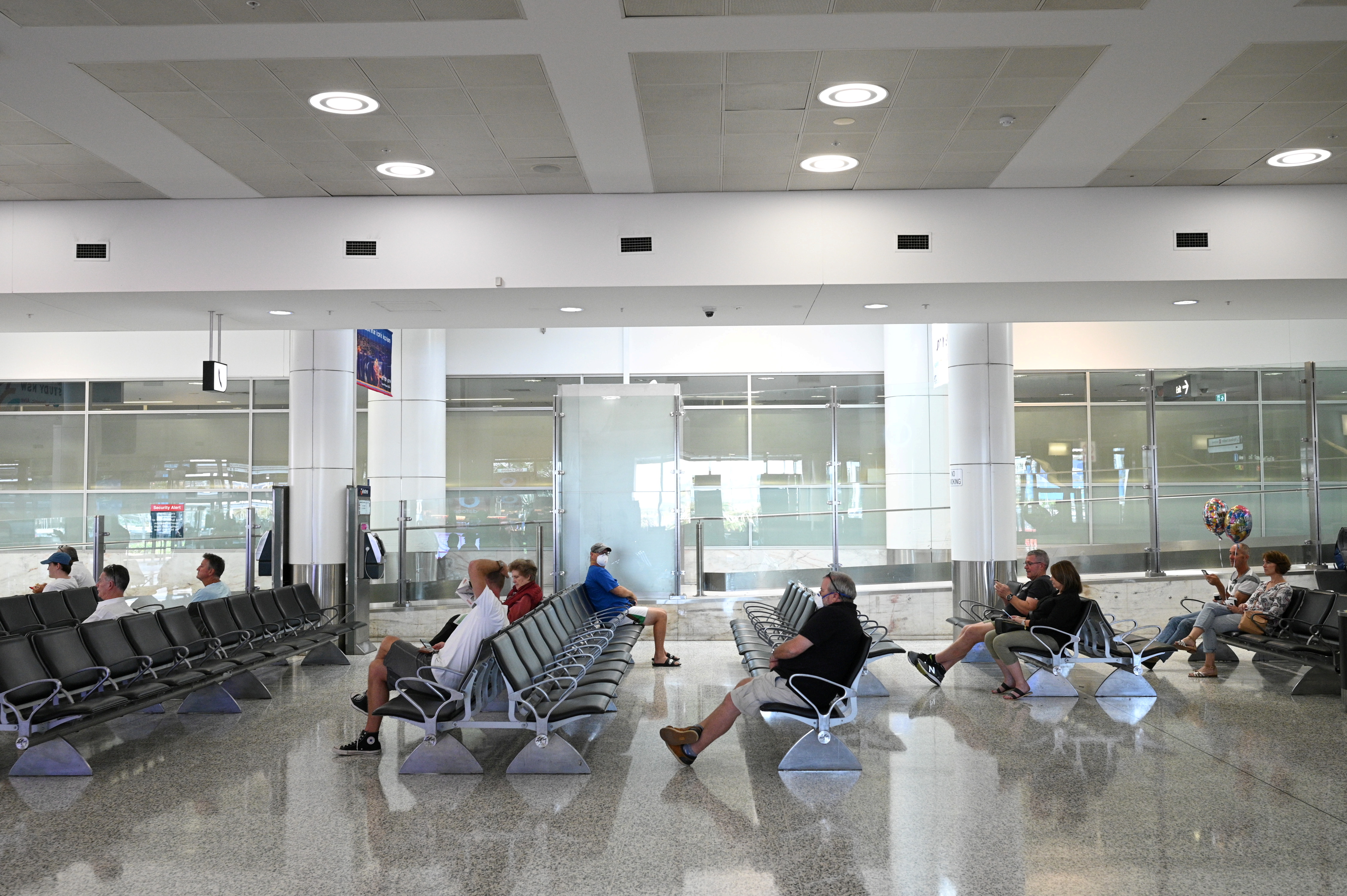 People sit in the arrivals section of the international terminal of Kingsford Smith International Airport the morning after Australia implemented an entry ban on non-citizens and non-residents intended to curb the spread of the coronavirus disease (COVID-19) in Sydney, Australia, March 21, 2020. REUTERS/Loren Elliott