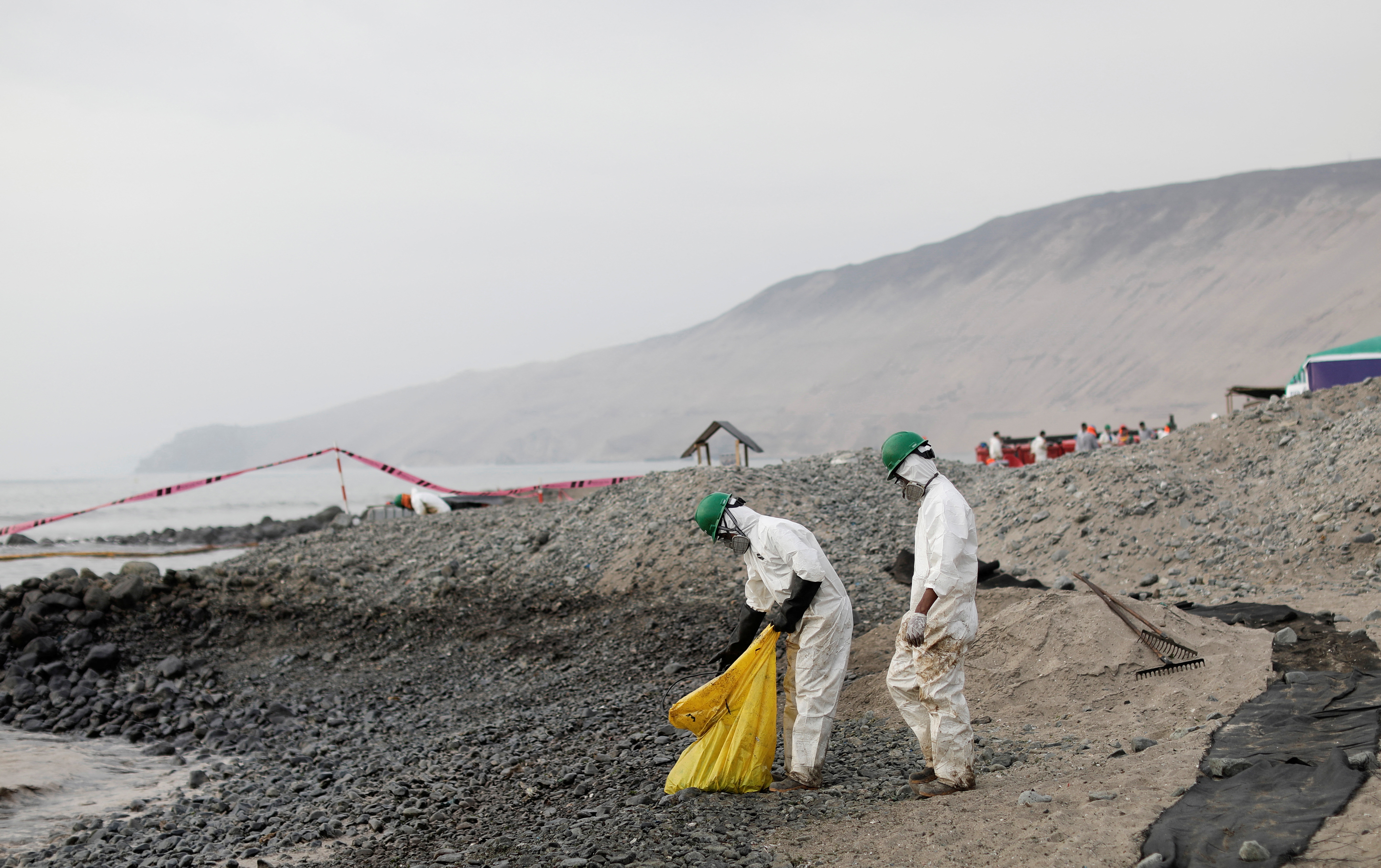 Workers clean up an oil spill at the beach as demonstrators take part in a protest outside Repsol's La Pampilla refinery in Ventanilla