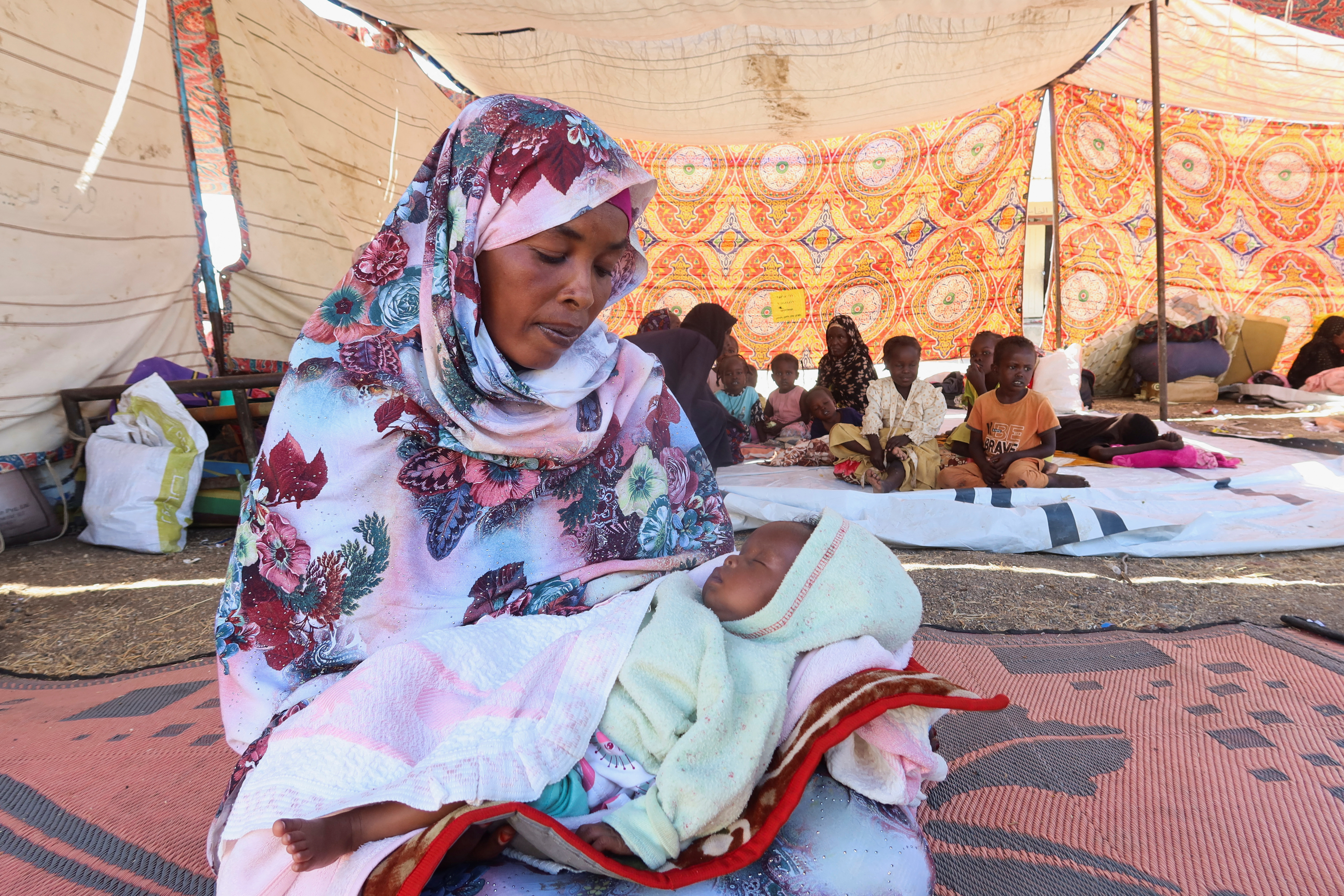 A Sudanese woman, Salwa Abdallah, displaced from Gezira state due to RSF violence, holds her baby as she sits in a tent in New Halfa