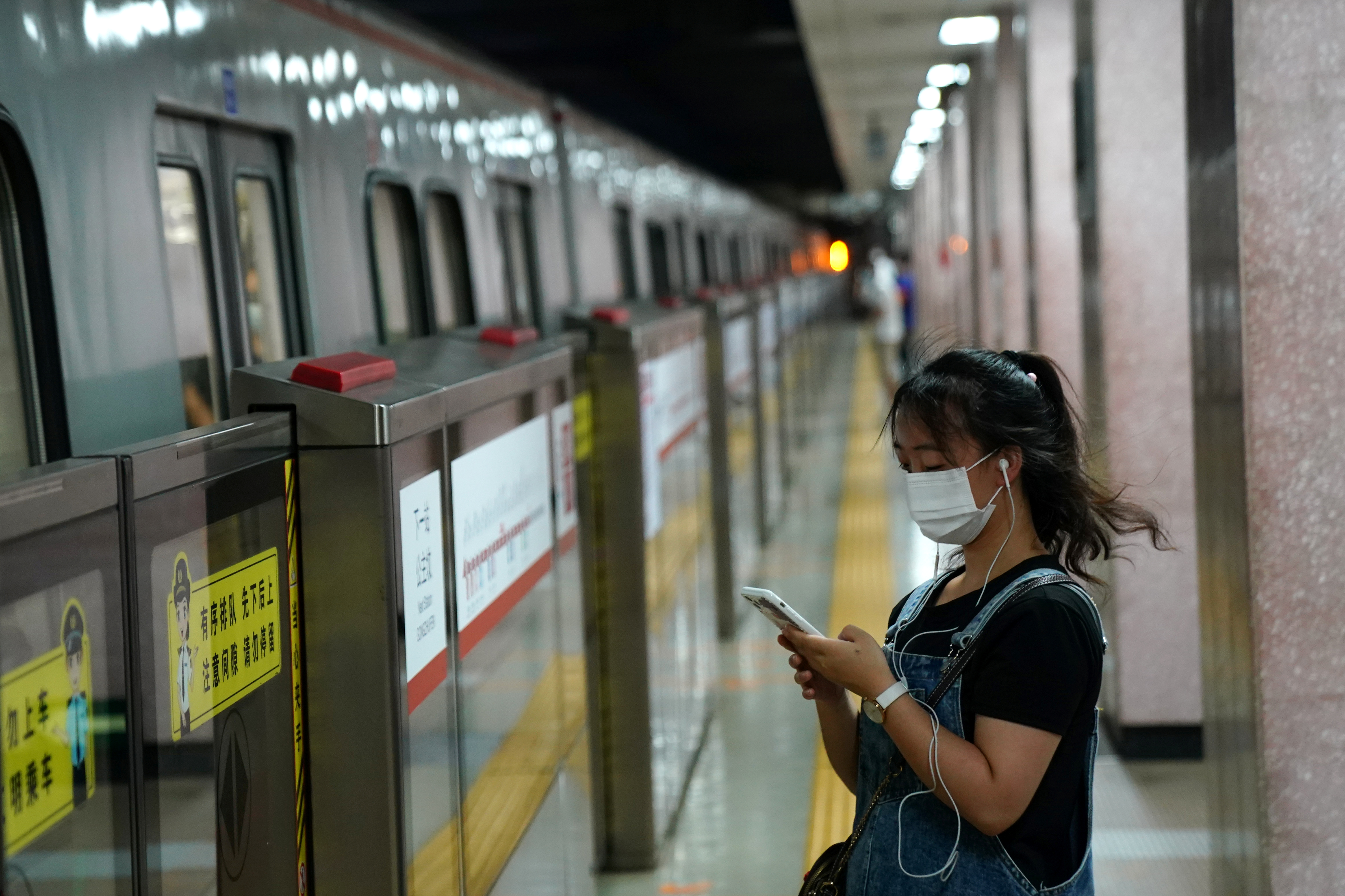 Woman wearing a face mask following  coronavirus disease (COVID-19) outbreak looks at her smartphone while waiting for a subway in Beijing