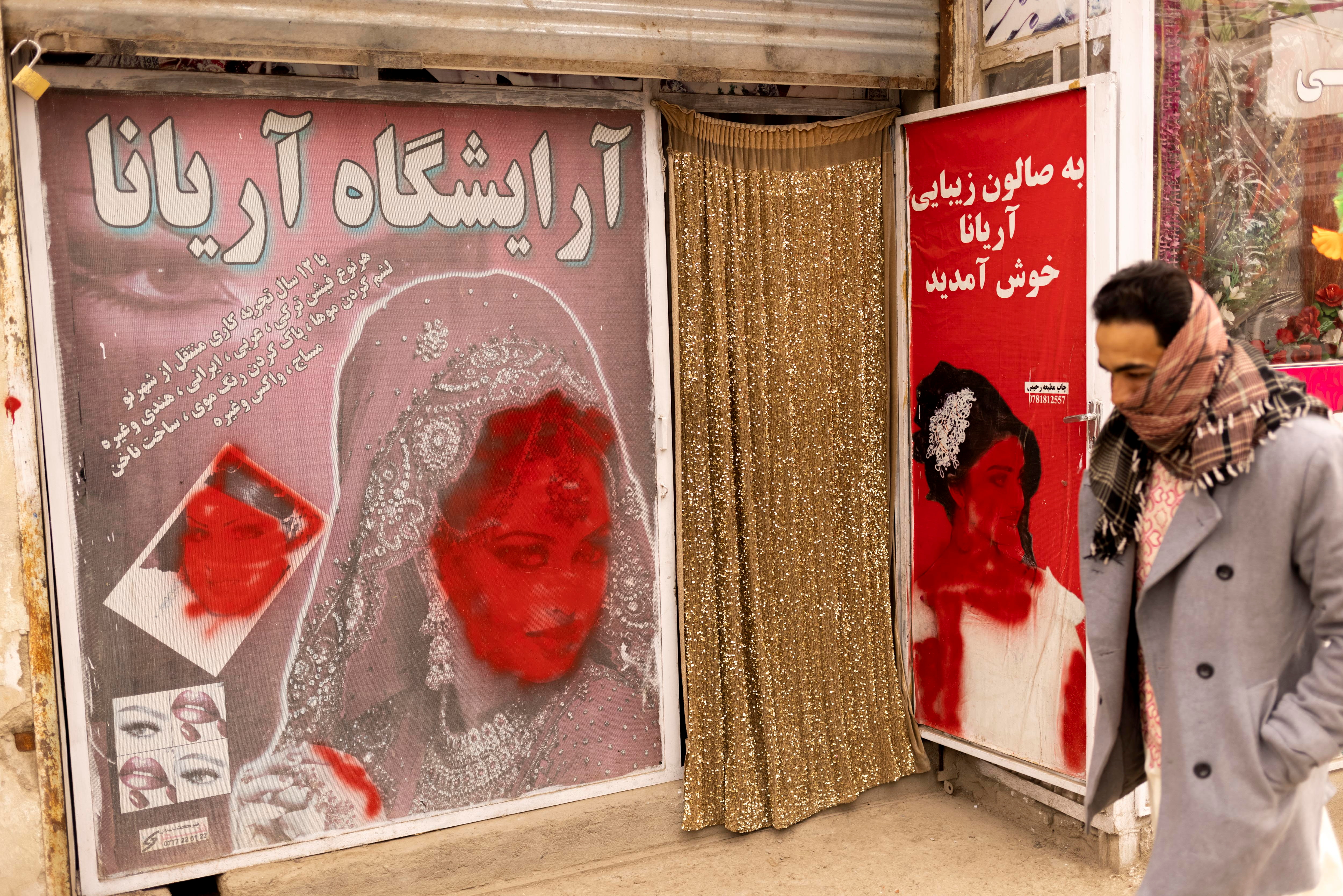 A man walks past a beauty shop with defaced pictures of women in Kabul, Afghanistan October 22, 2021. REUTERS/Jorge Silva