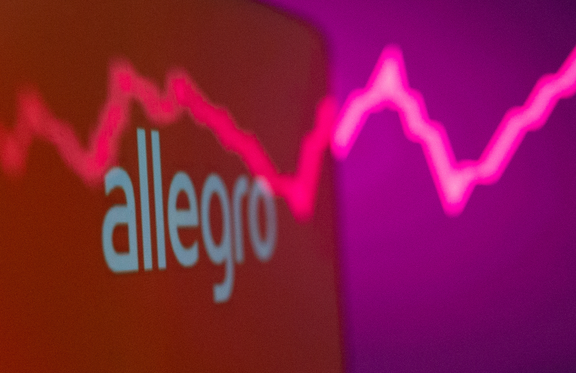 Allegro logo is seen on a smartphone in front of a displayed stock graph in this illustration
