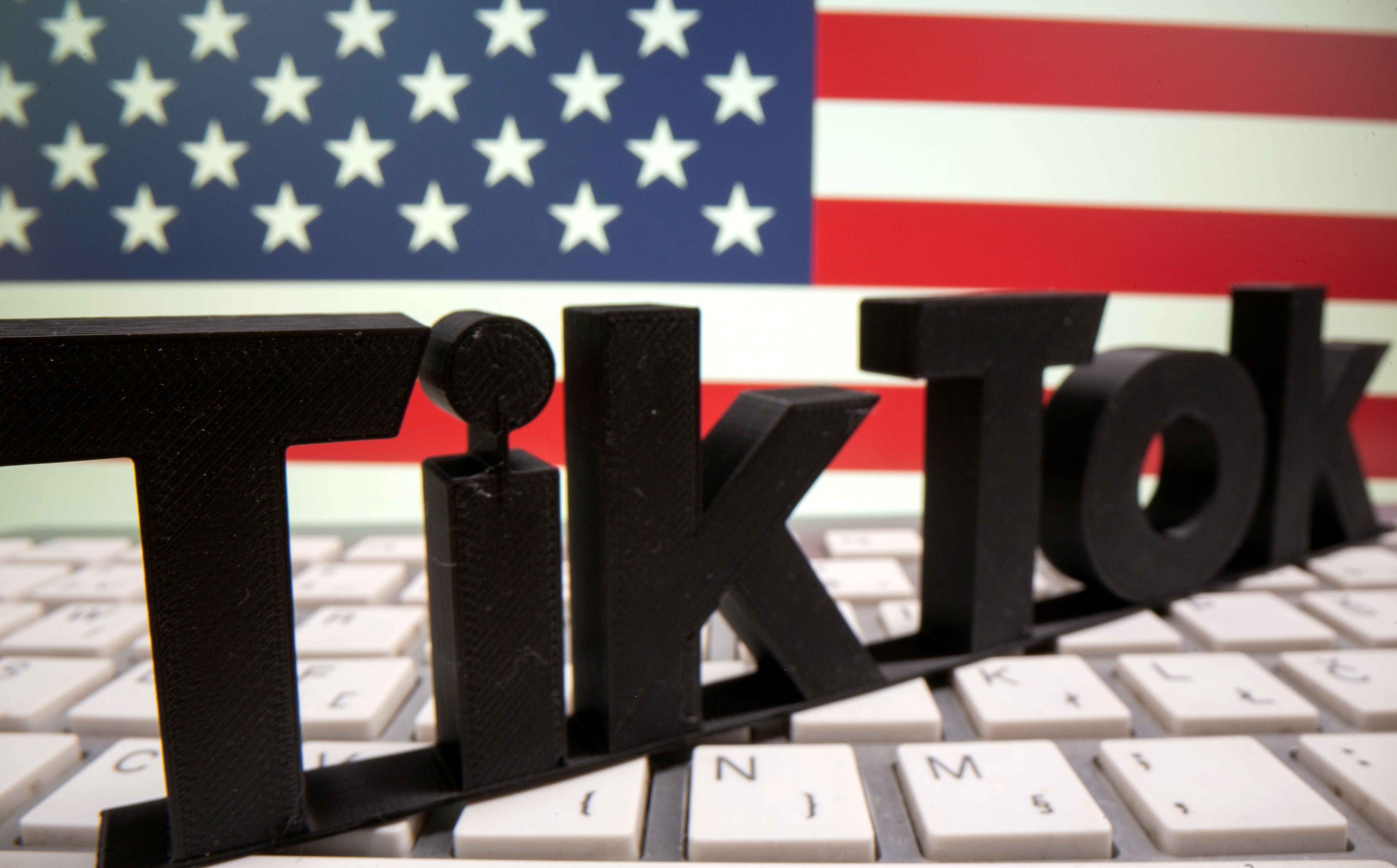 A 3D printed Tik Tok logo is placed on a keyboard in front of U.S. flag in this illustration