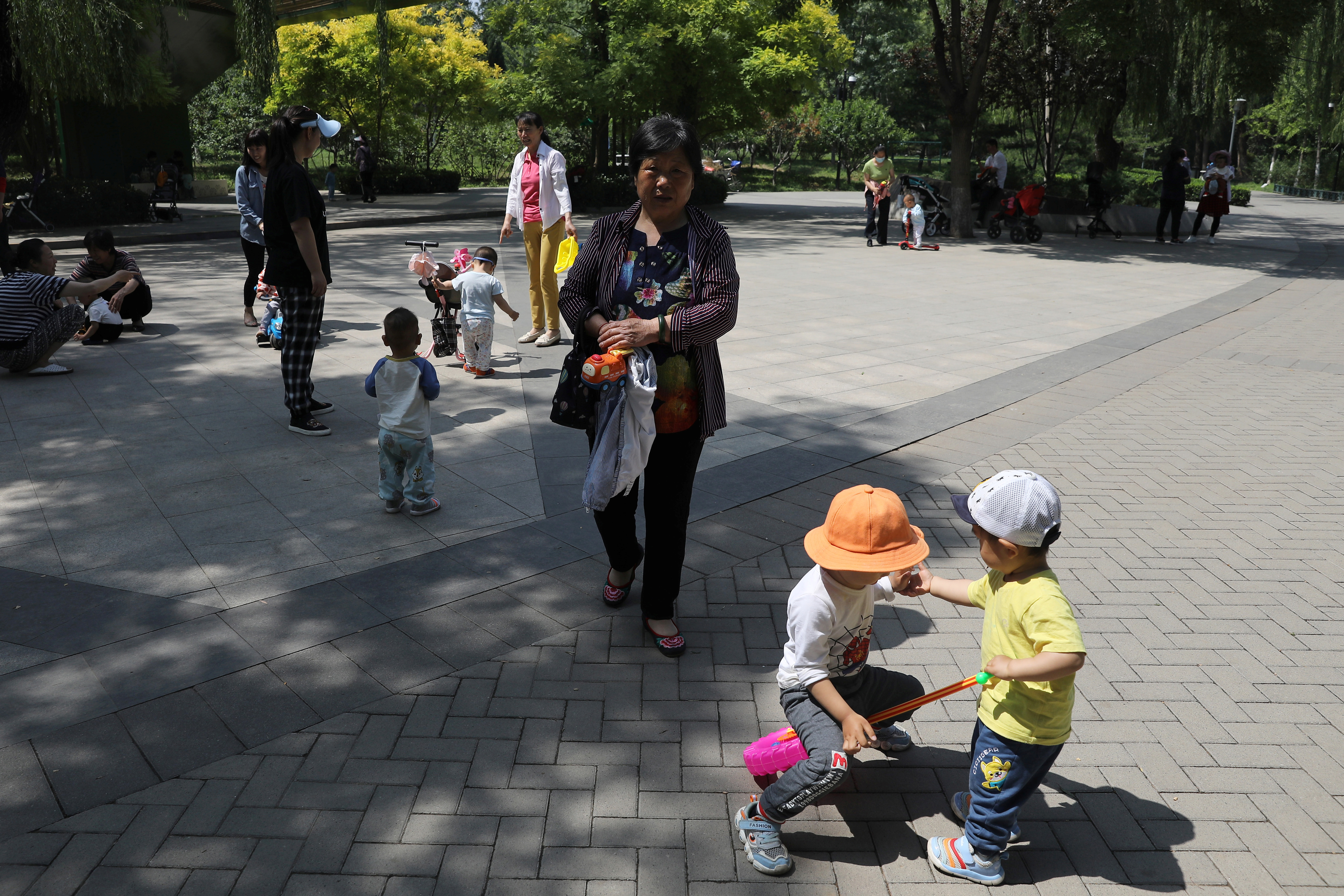 Children play next to adults at a park in Beijing