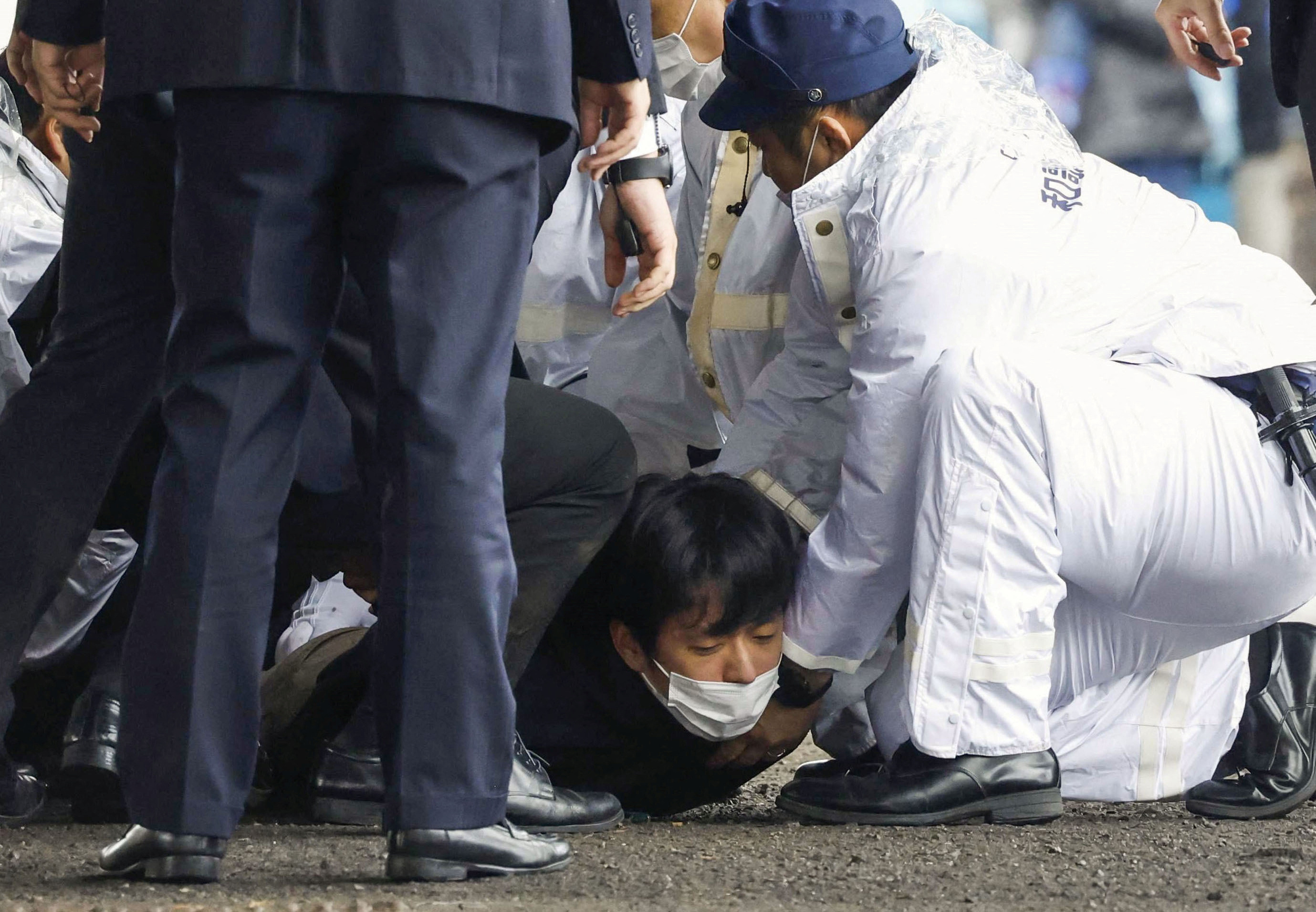 A man, believed to be a suspect who threw a pipe-like object near Japanese Prime Minister Fumio Kishida during his outdoor speech, is held by police officers in Wakayama
