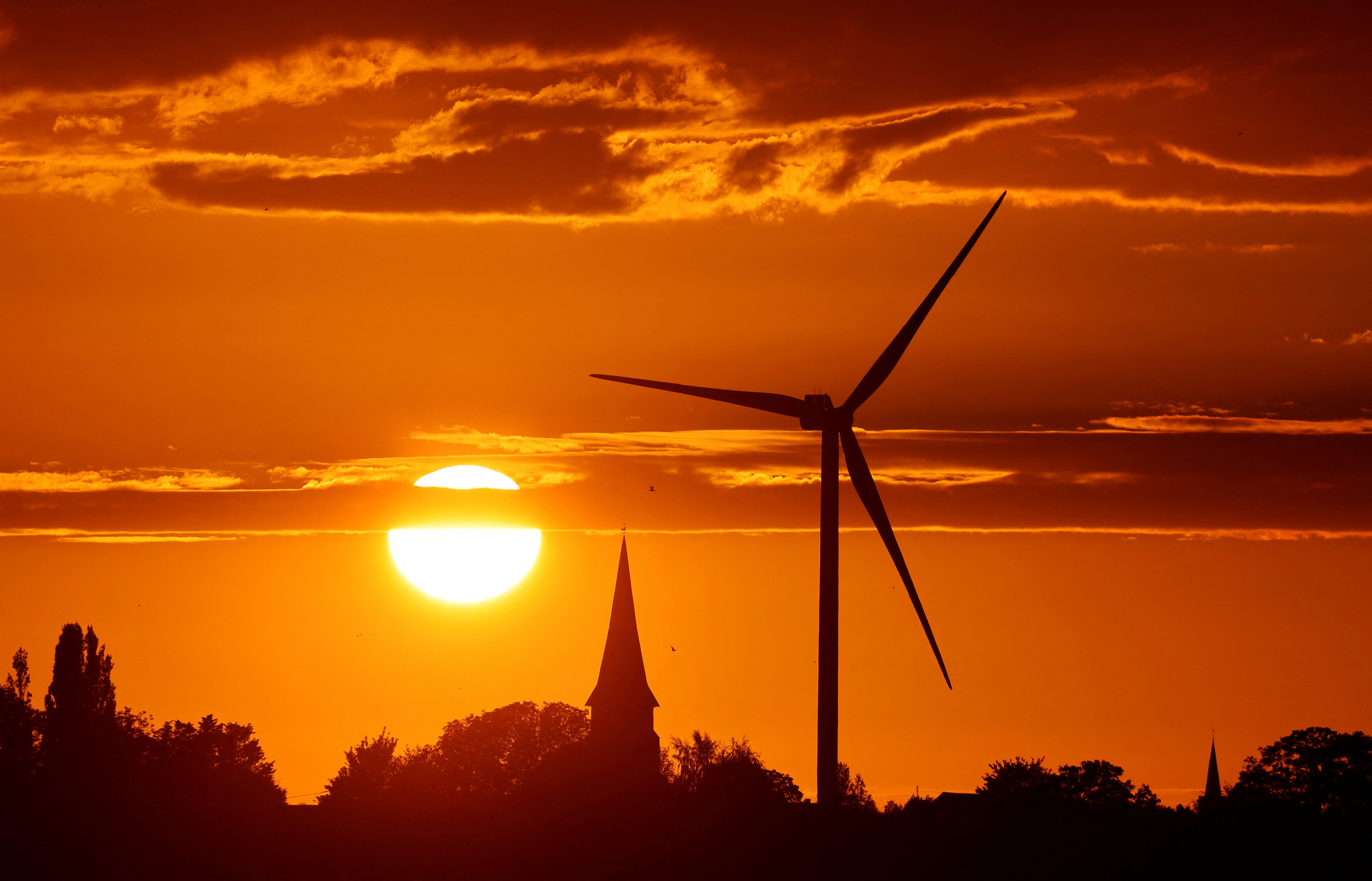A power-generating windmill turbine and the church of the village are pictured during sunset at a wind park in Ecoust-Saint-Mein
