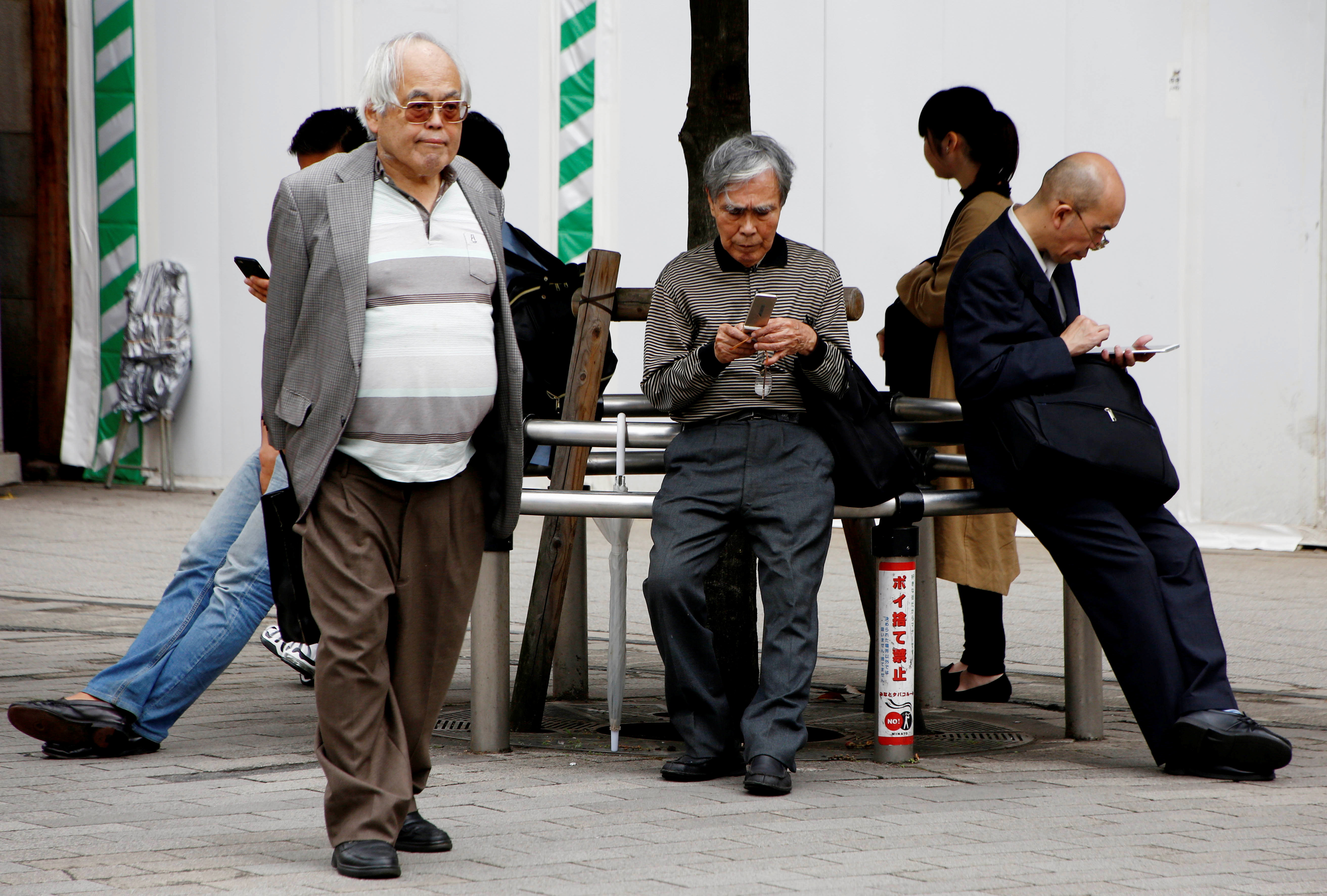 An elderly man uses a mobile phone in front a station in Tokyo