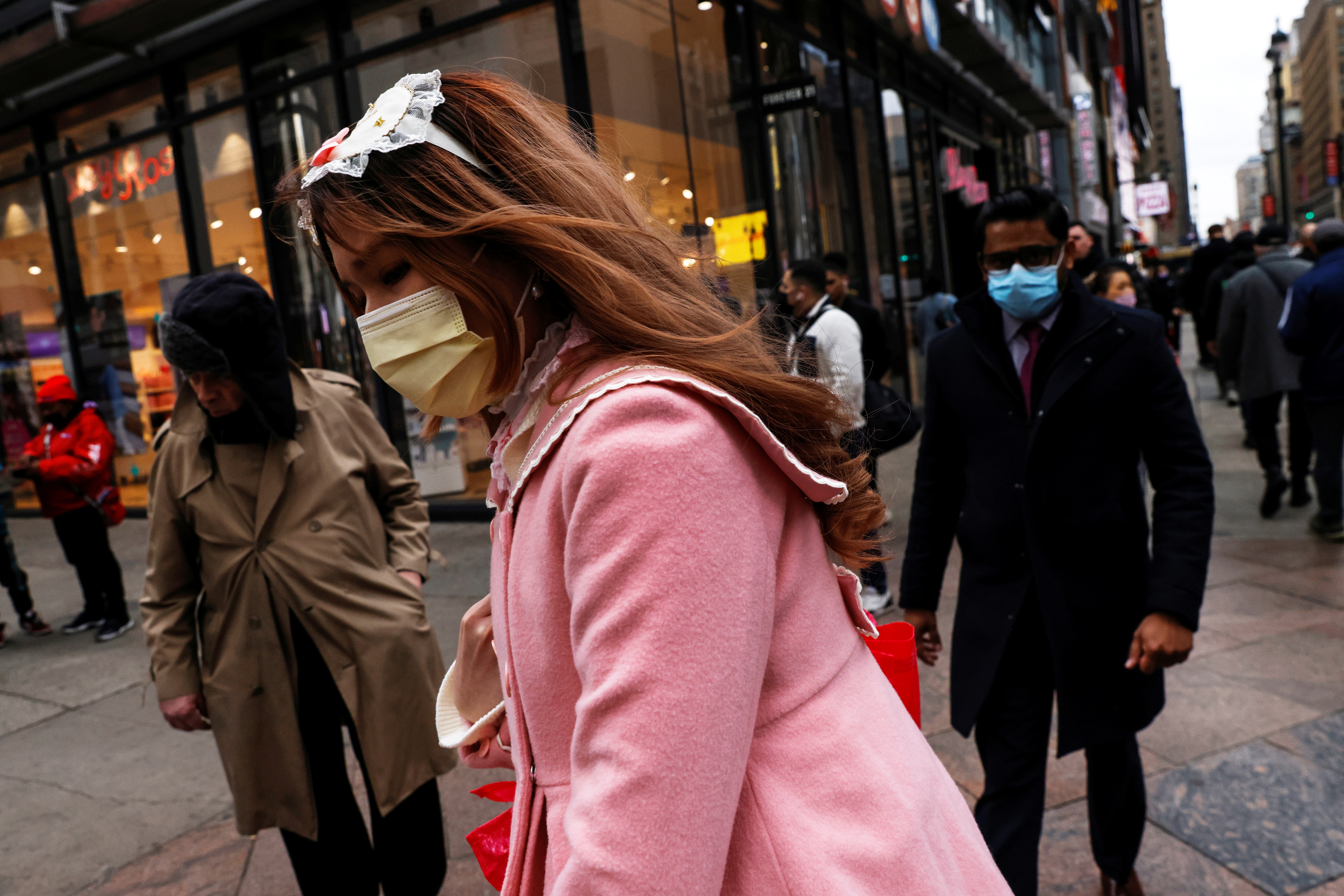 A woman wearing a protective face mask, amid the coronavirus disease (COVID-19) pandemic, walks by pedestrians along 34th street outside Pennsylvania Station in New York City, U.S., November 22, 2021.  REUTERS/Shannon Stapleton