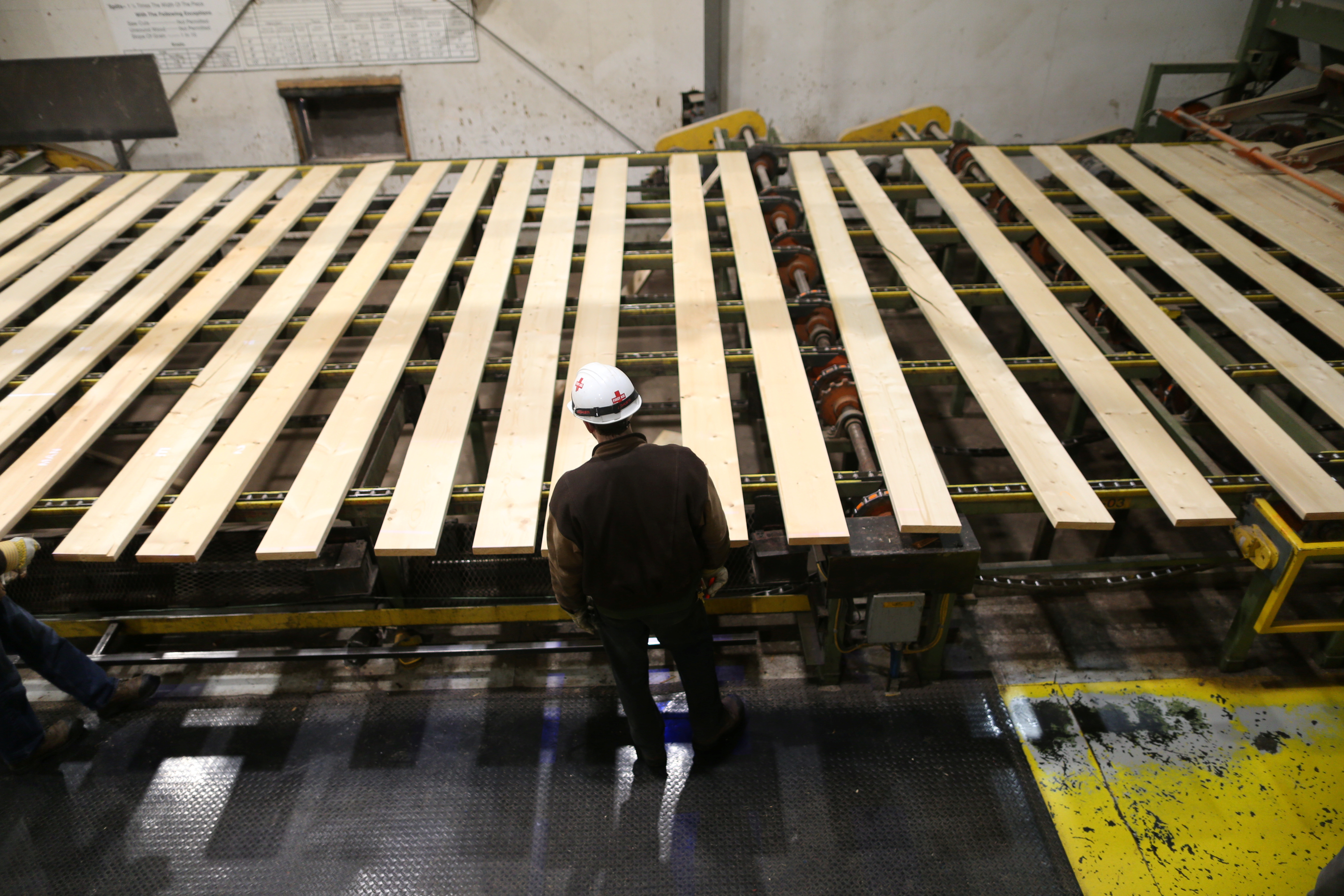 A worker inspects lumber on a conveyor belt at West Fraser Pacific Inland Resources sawmill in Smithers