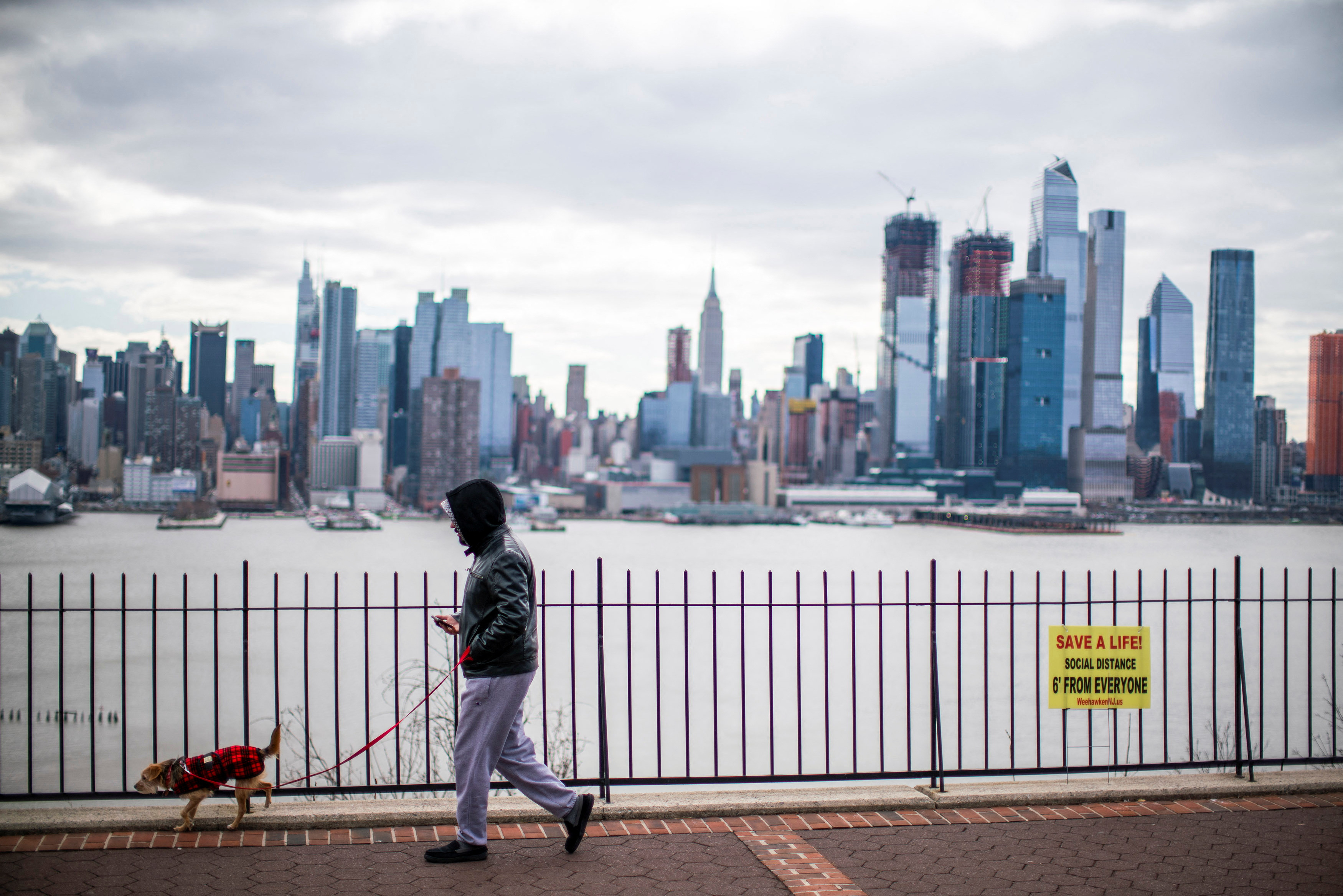 A man walks his dog without wearing a face mask during the coronavirus disease (COVID-19) pandemic, while the Empire State Building and New York skyline are seen from Weehawken, in New Jersey