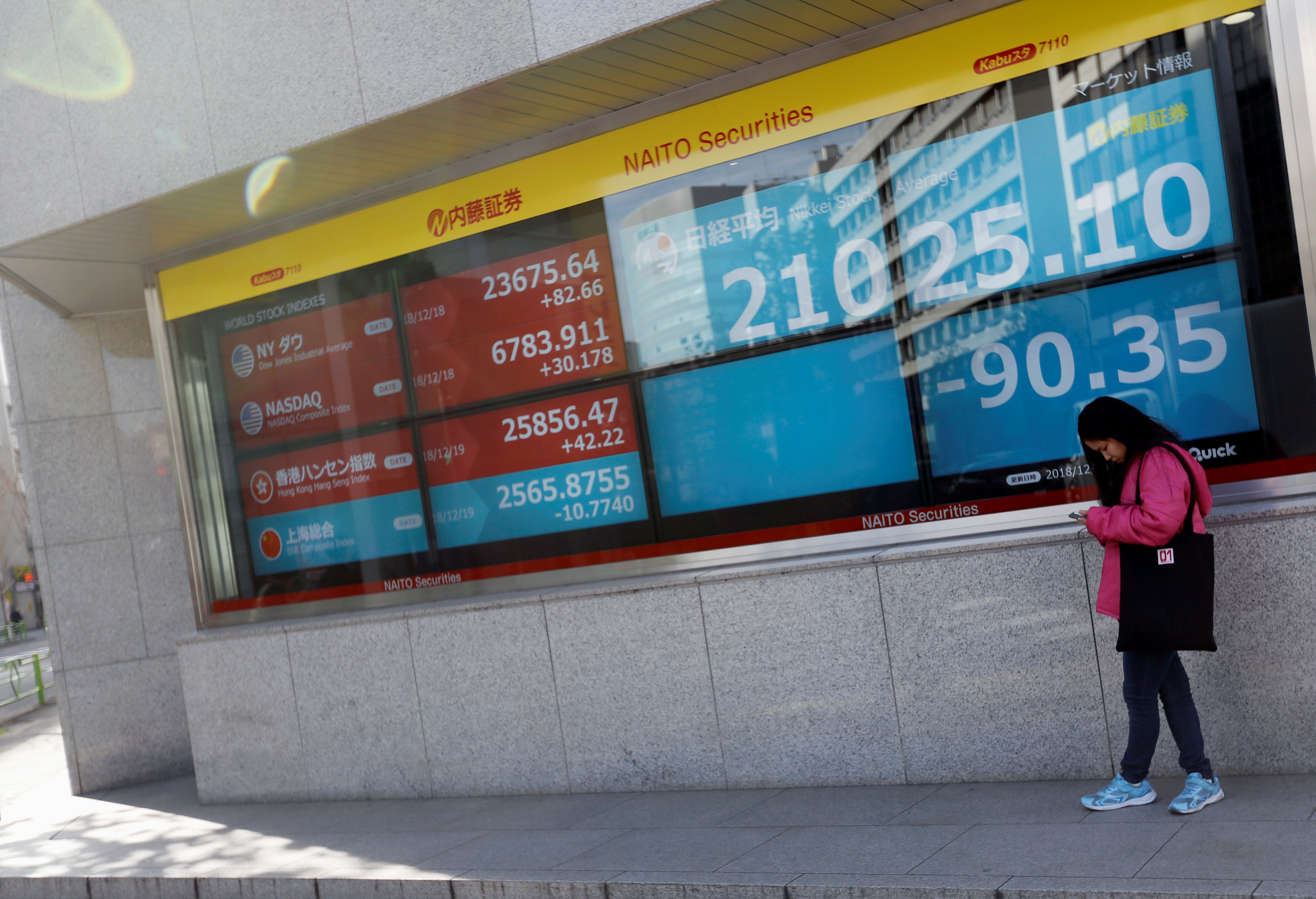 A woman stands in front of a screen displaying Japan's Nikkei share average, U.S. and other countries' stock market indicators outside a brokerage in Tokyo