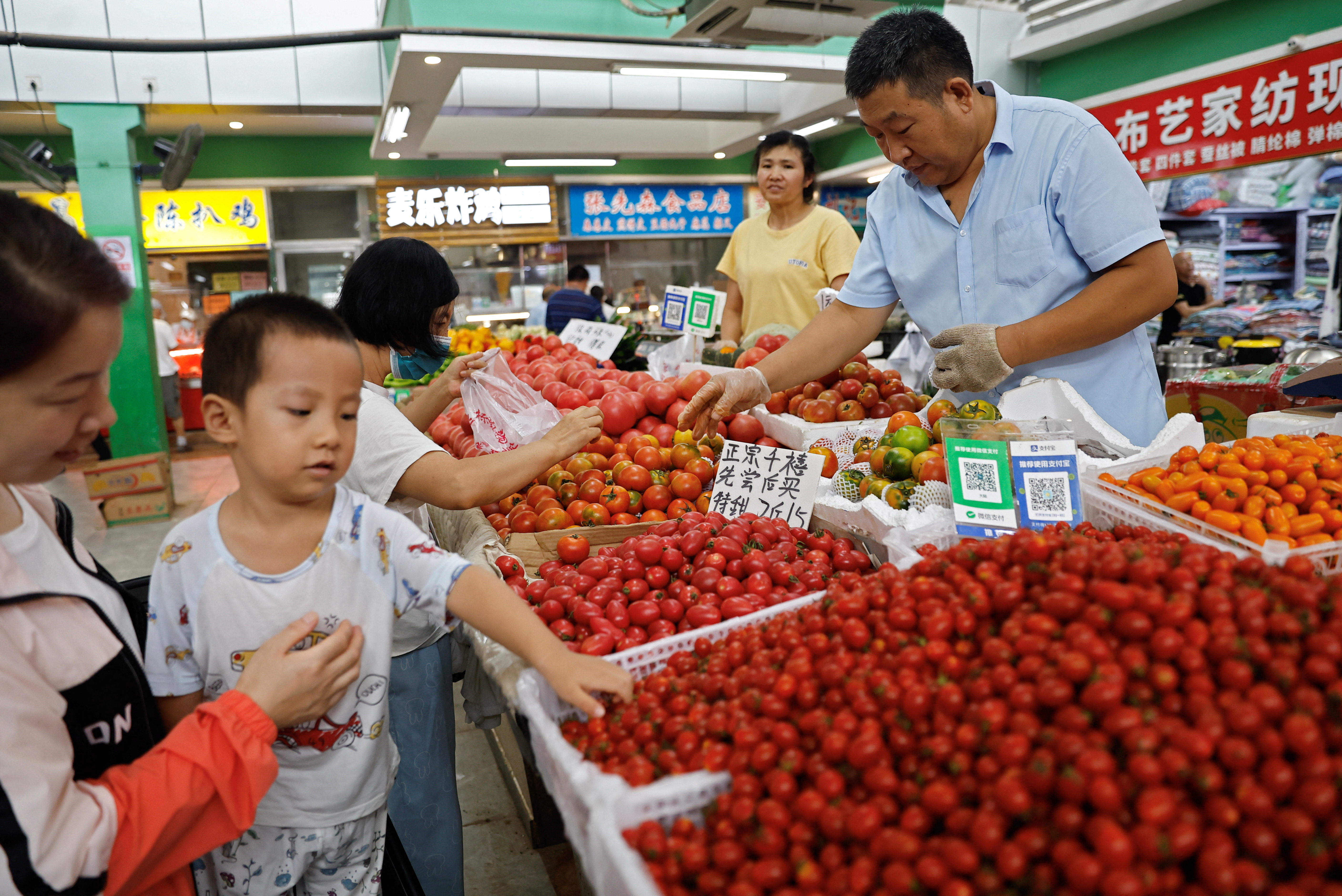 Clientes colhem tomates em uma barraca dentro de um mercado matinal em Pequim