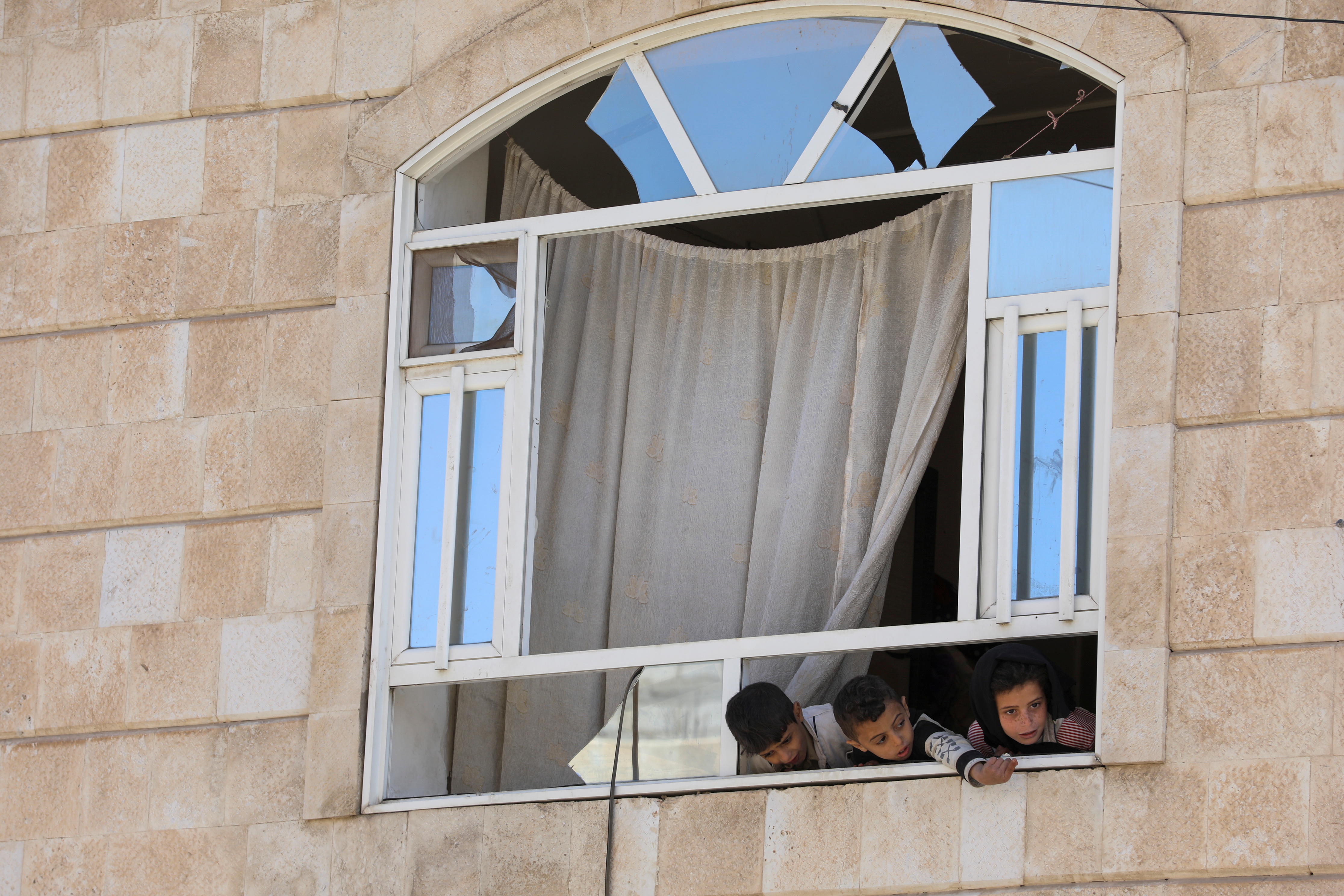 Children look from the window of their apartment in a building near a car workshop hit by a Saudi-led air strike, in Sanaa