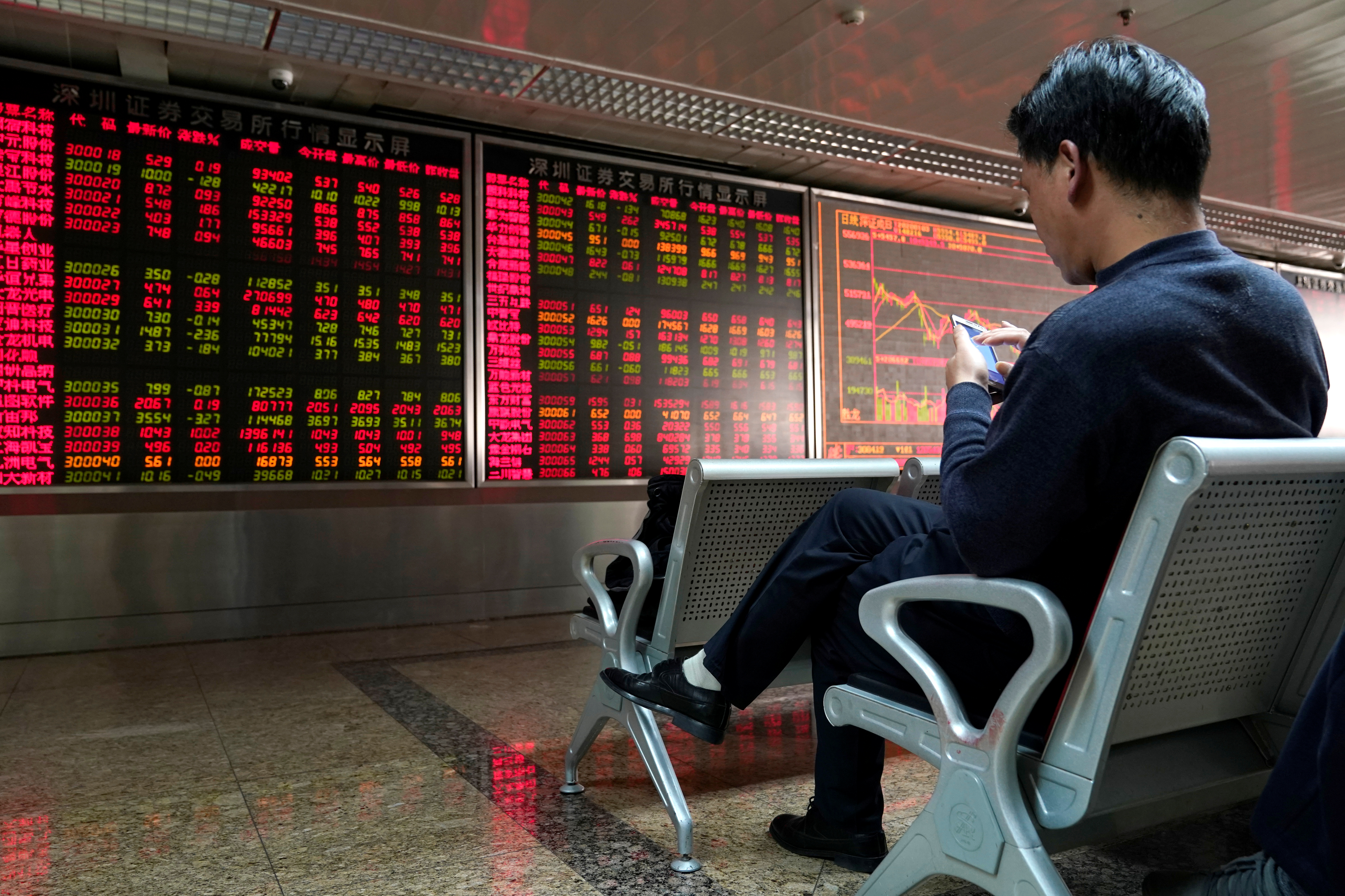 An investor uses his mobile phone in front of a stock quotation board at a brokerage office in Beijing