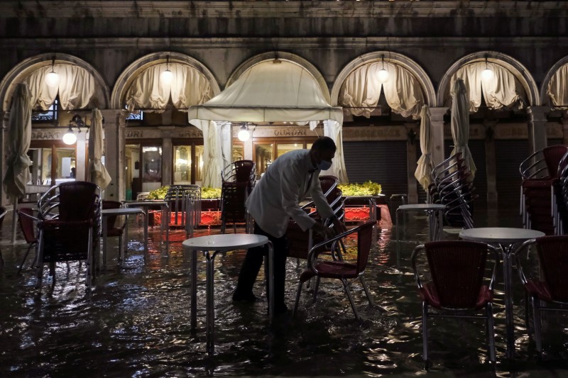 A worker closes a restaurant in a flooded St. Mark's Square during an exceptional high water in Venice, Italy August 8, 2021. Picture taken August 8, 2021. REUTERS/Manuel Silvestri
