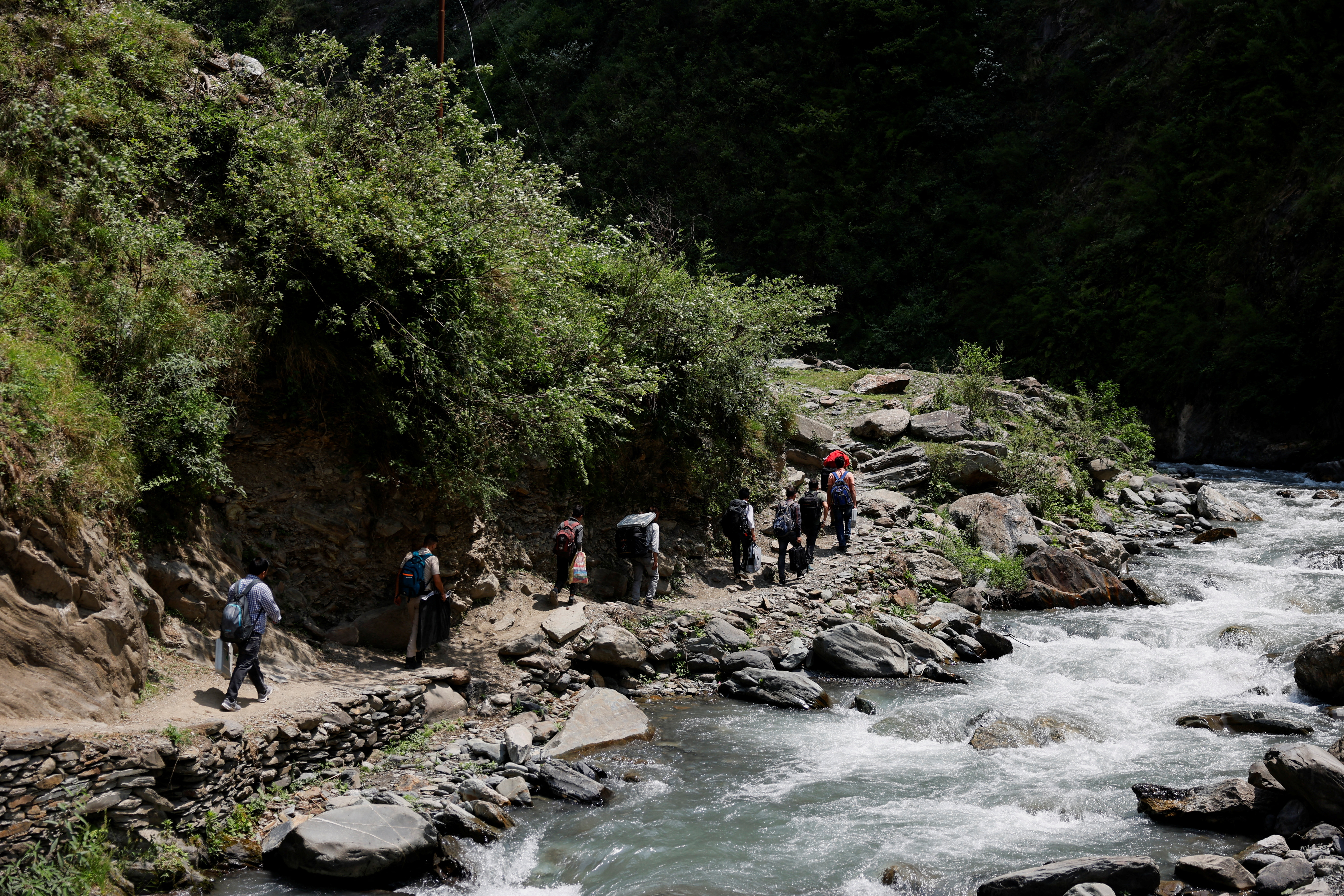 Election officials and porters carrying VVPAT and EVM machines walk past a river during a trek in the mountains to reach a remote polling station, ahead of the seventh and final phase of the elections, in Almi