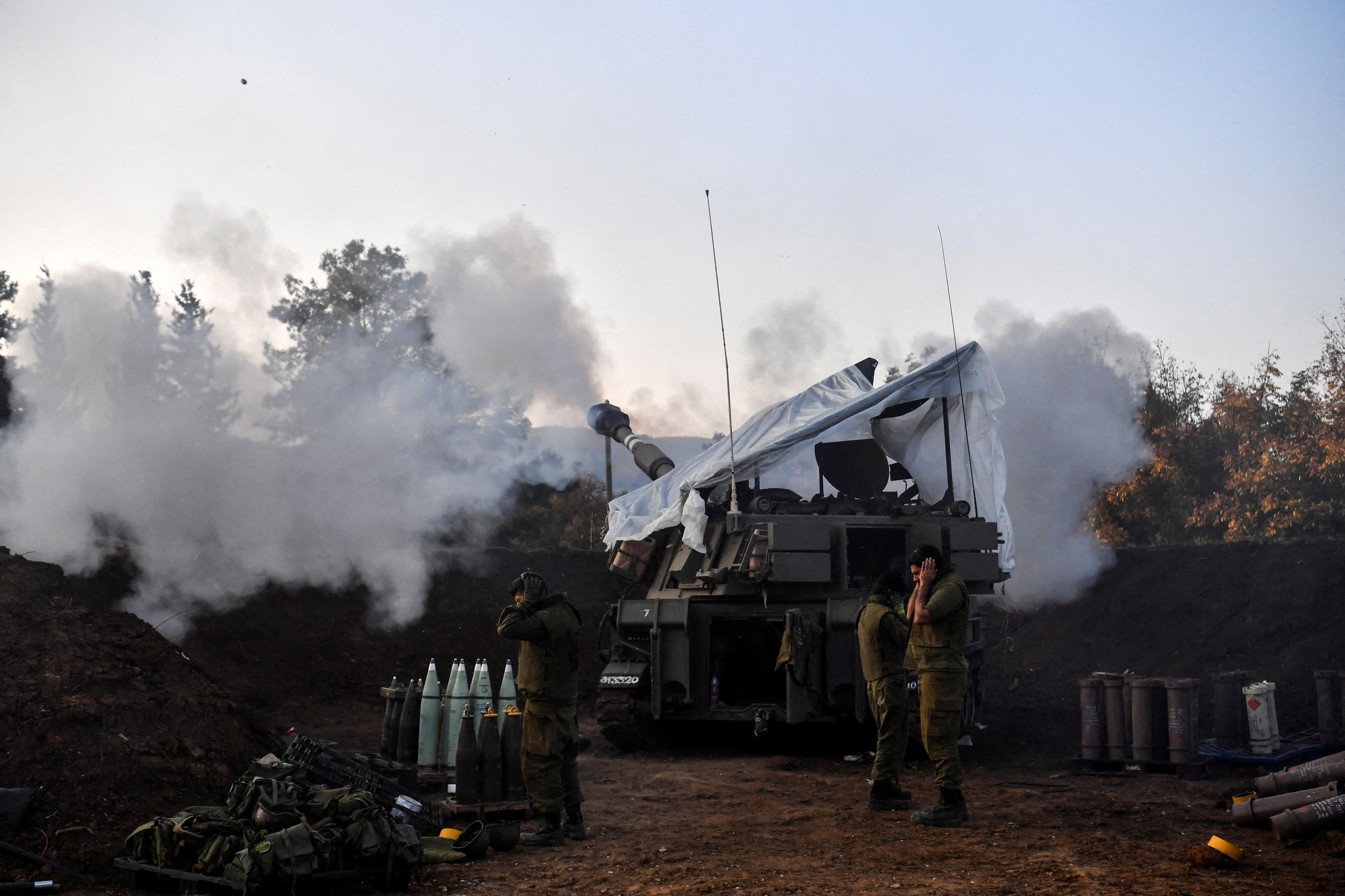 Israeli soldiers stand by, as a mobile artillery unit fires, on the Israeli side of the Israel-Lebanon border